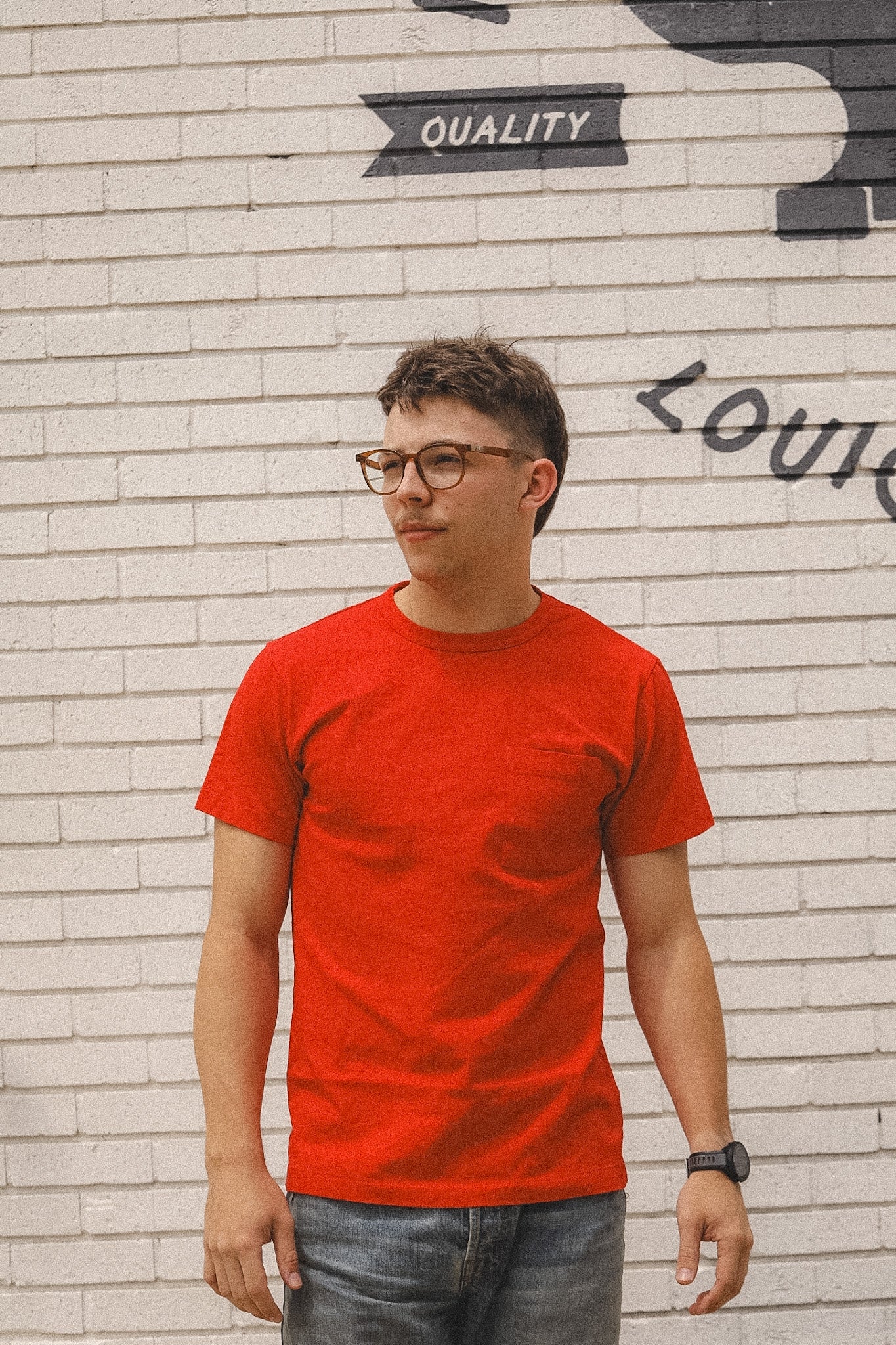 Person wearing a red t-shirt standing in front of a textured wall with graffiti.