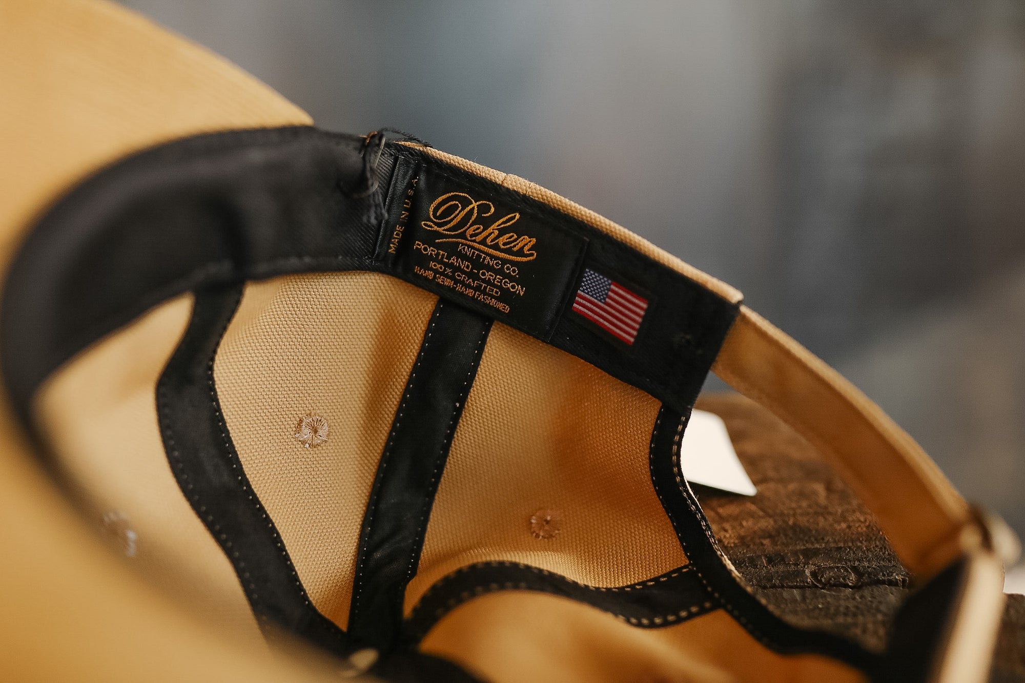 Close-up of a beige cap with a black strap and 'Belen' branding on a blurred background