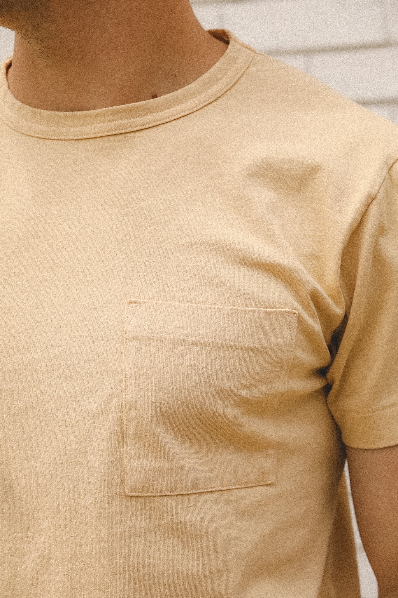 Close-up of a beige t-shirt with a pocket on a neutral background