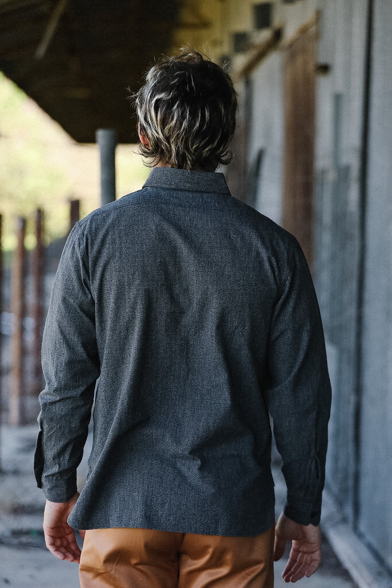 Person wearing a dark gray shirt and brown pants walking away from the camera.