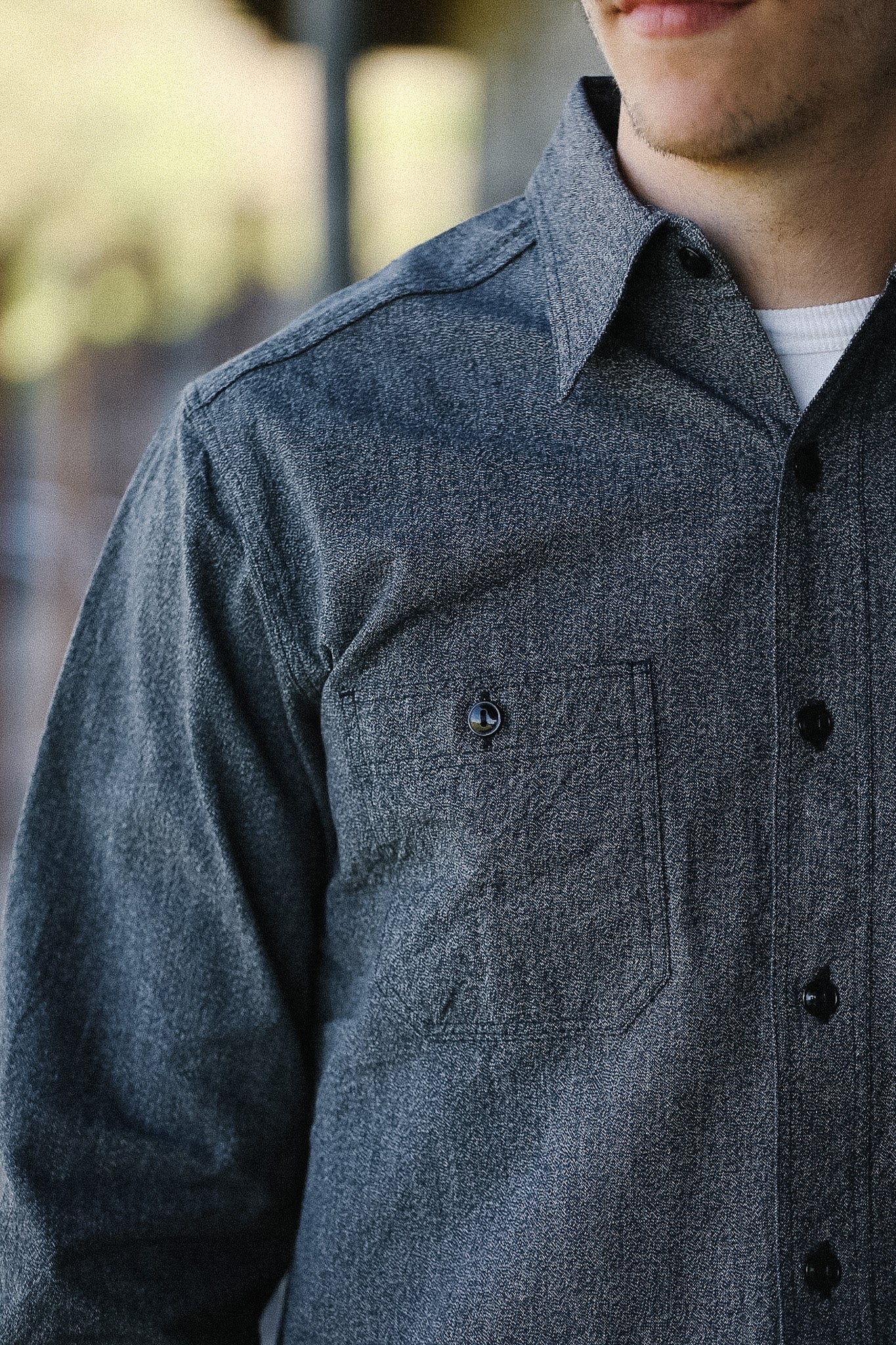 Close-up of a person wearing a gray button-up shirt with a blurred background