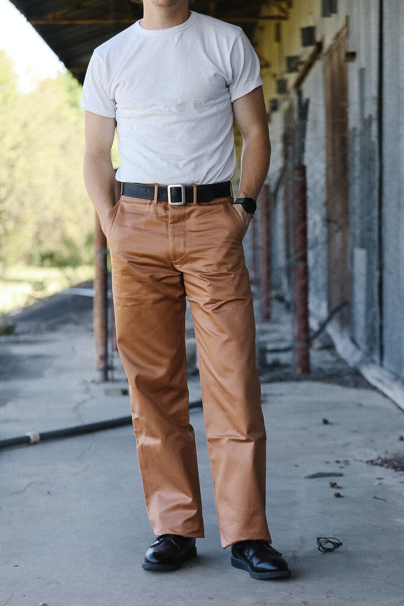 Person wearing a white t-shirt and brown pants standing outdoors.