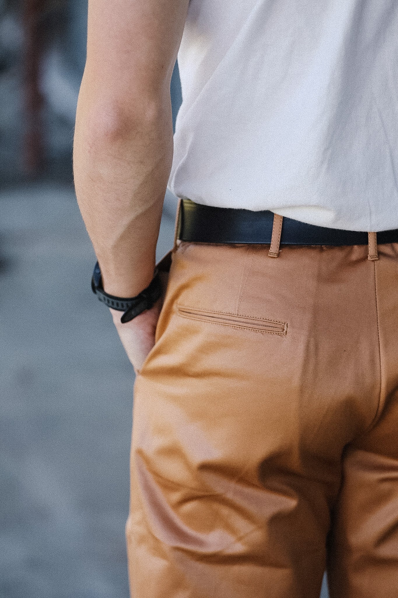 Person wearing a white shirt, brown pants, and a black belt with a blurred background