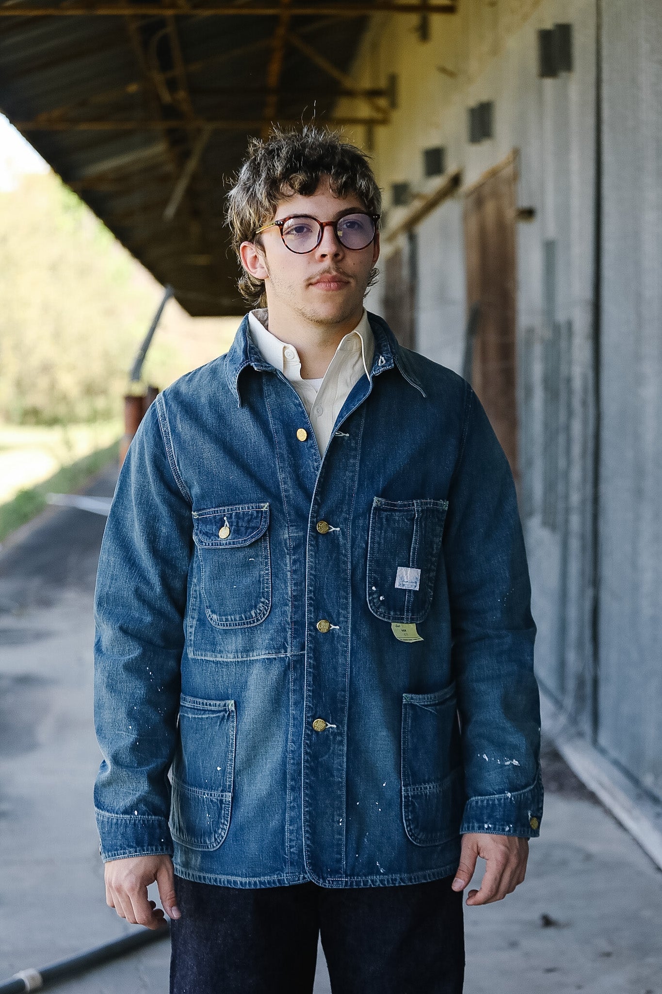 Person wearing a blue denim jacket standing outdoors under a shelter.
