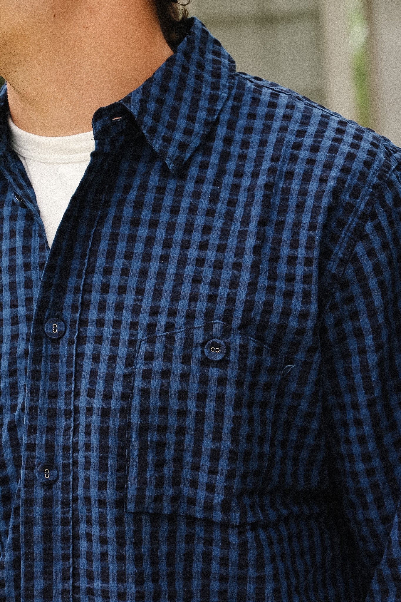 Close-up of a person wearing a blue and black checkered button-up shirt over a white undershirt.
