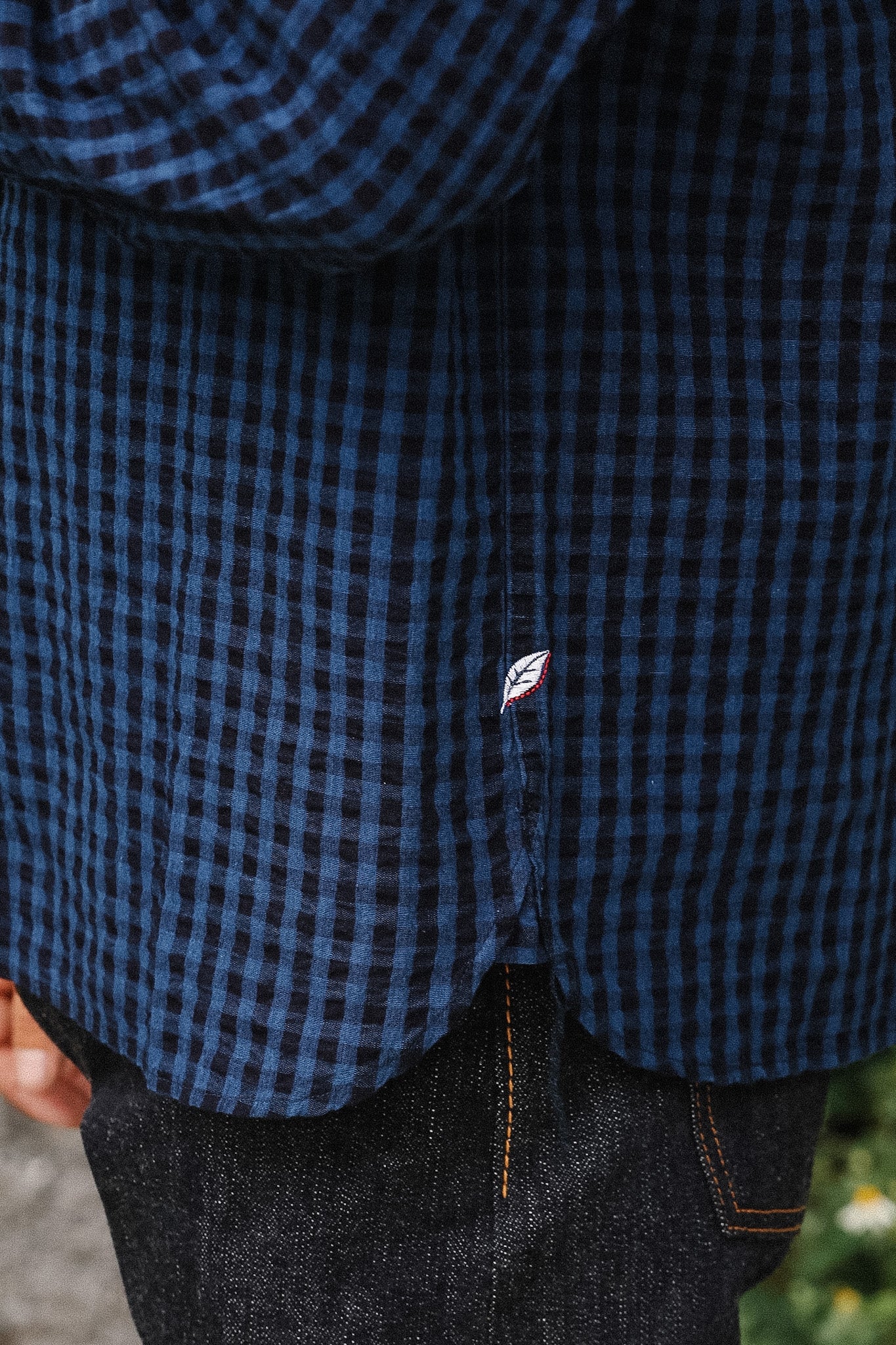 Close-up of a person wearing a dark blue and black gingham plaid button-up shirt with dark denim jeans.
