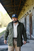 Man wearing a green jacket and cap standing in an industrial setting