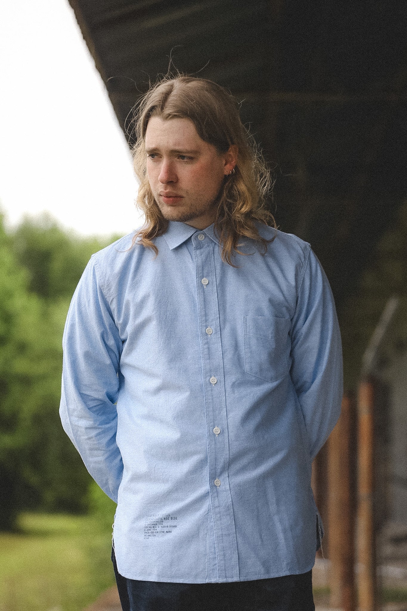 Man wearing a light blue button-up shirt outdoors with greenery in the background