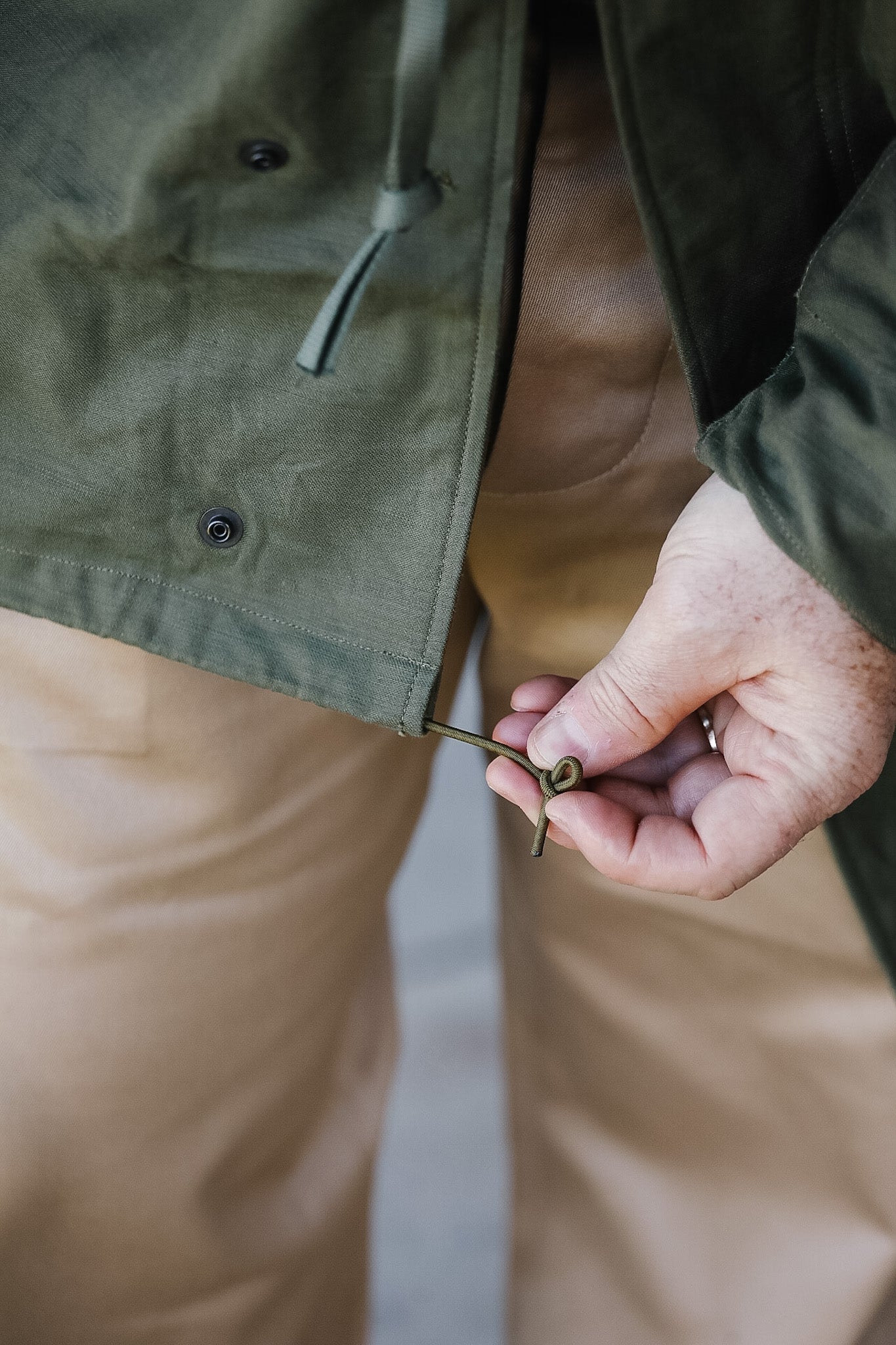 Person wearing a green jacket and beige pants, holding a key.
