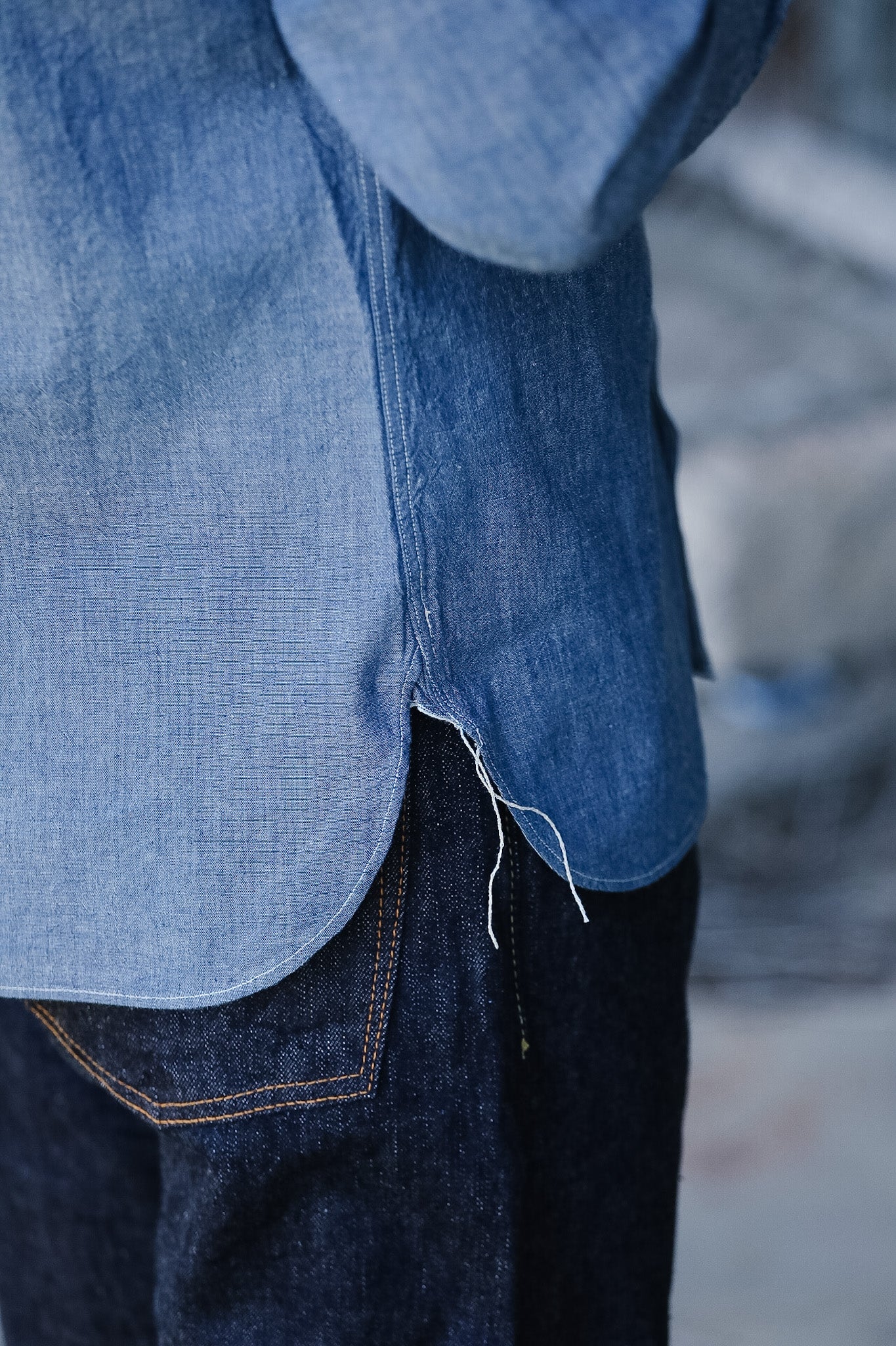 Close-up of a person wearing a blue denim shirt and jeans with a blurred background.