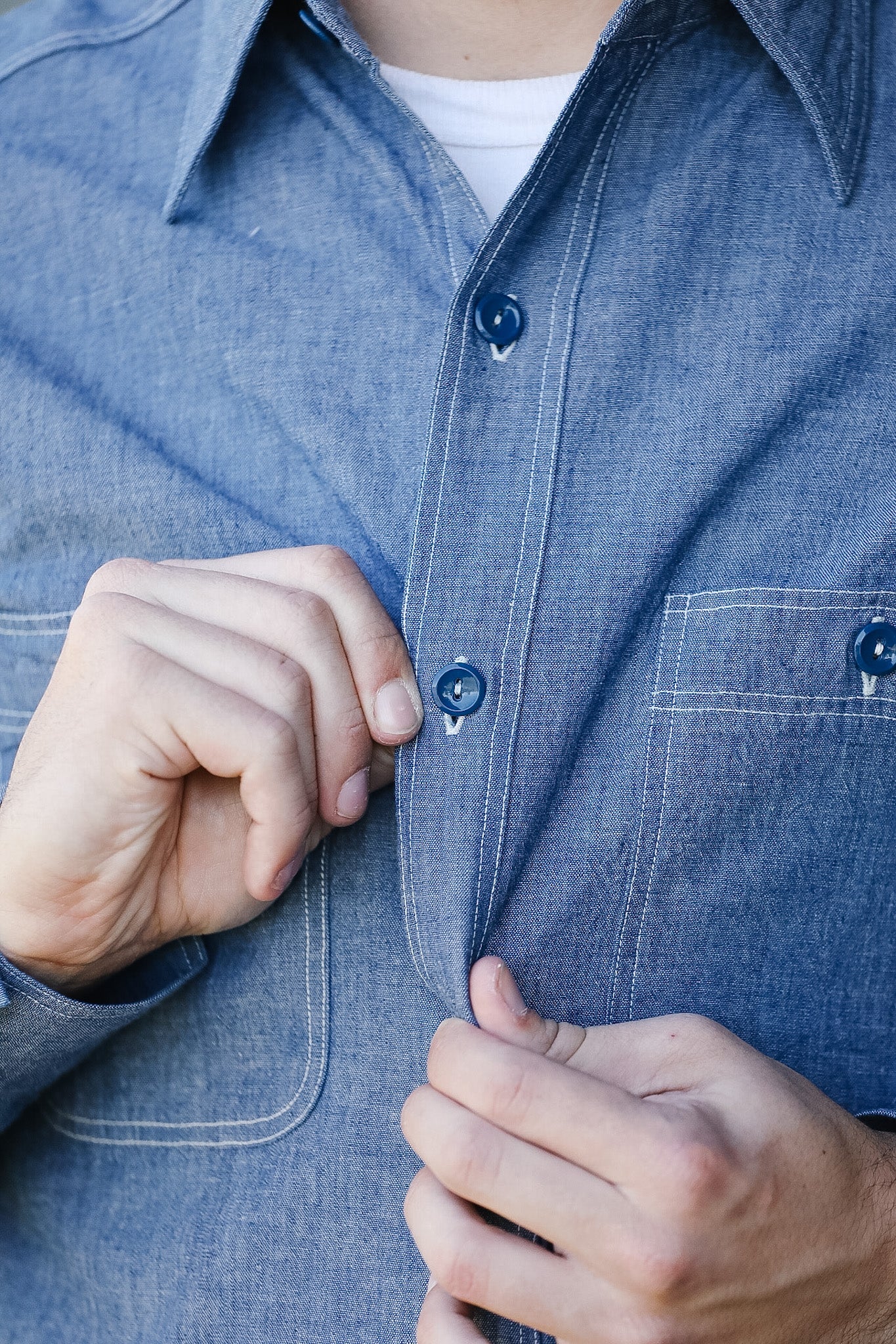 Person buttoning a blue denim shirt with a close-up of hands