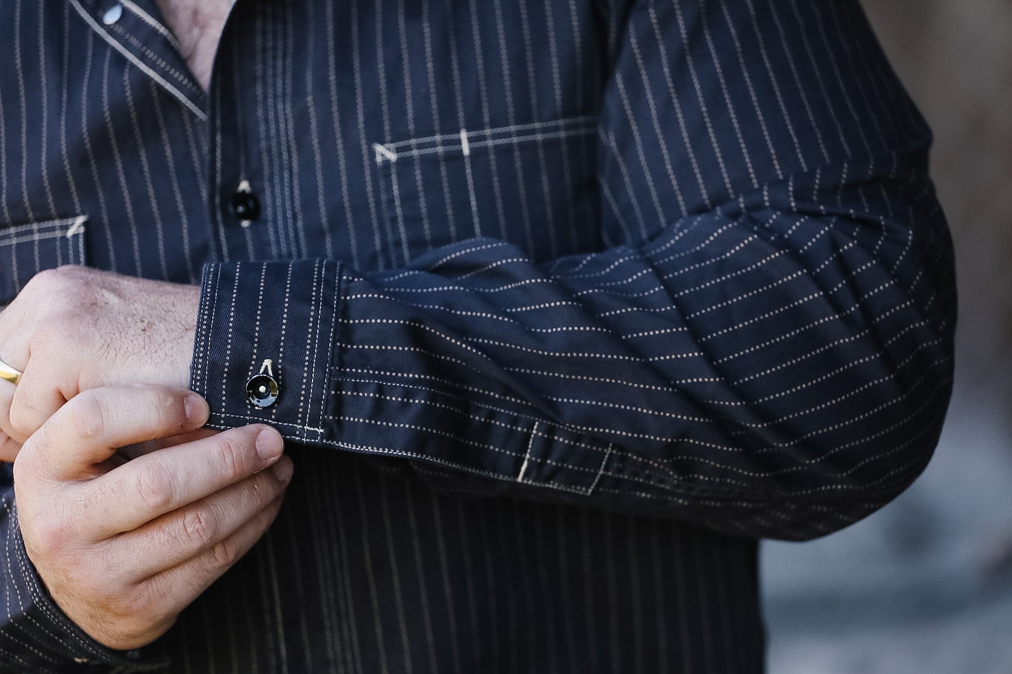 Close-up of a person wearing a dark pinstripe shirt with rolled-up sleeve.