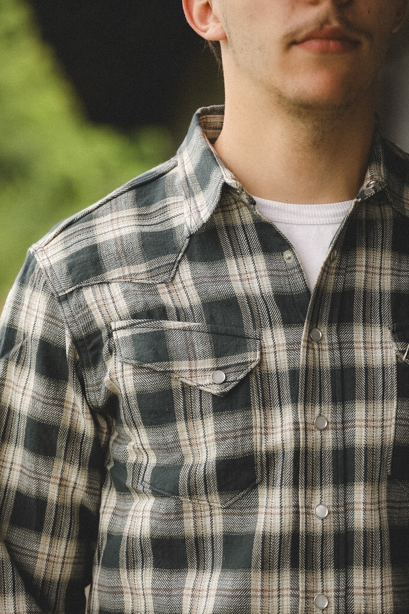 Person wearing a plaid shirt with a blurred natural background