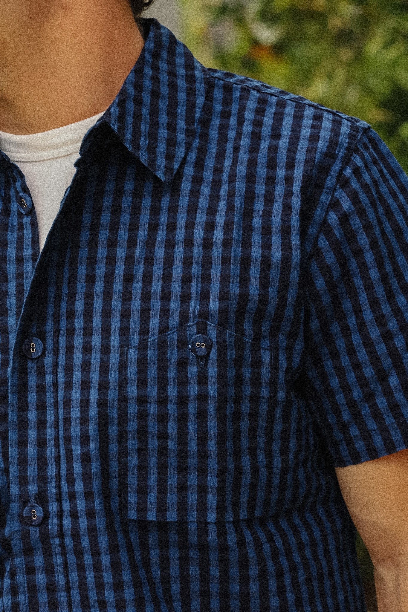 Close-up of a person wearing a short-sleeve button-up shirt with a blue and black gingham pattern, layered over a white undershirt.