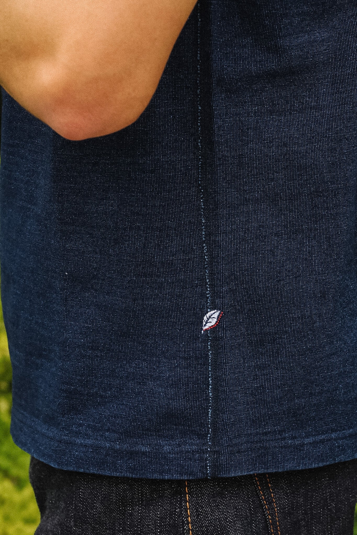 Close-up of a person wearing a dark navy blue ribbed knit top, showing the side seam and a small embroidered logo near the hem.