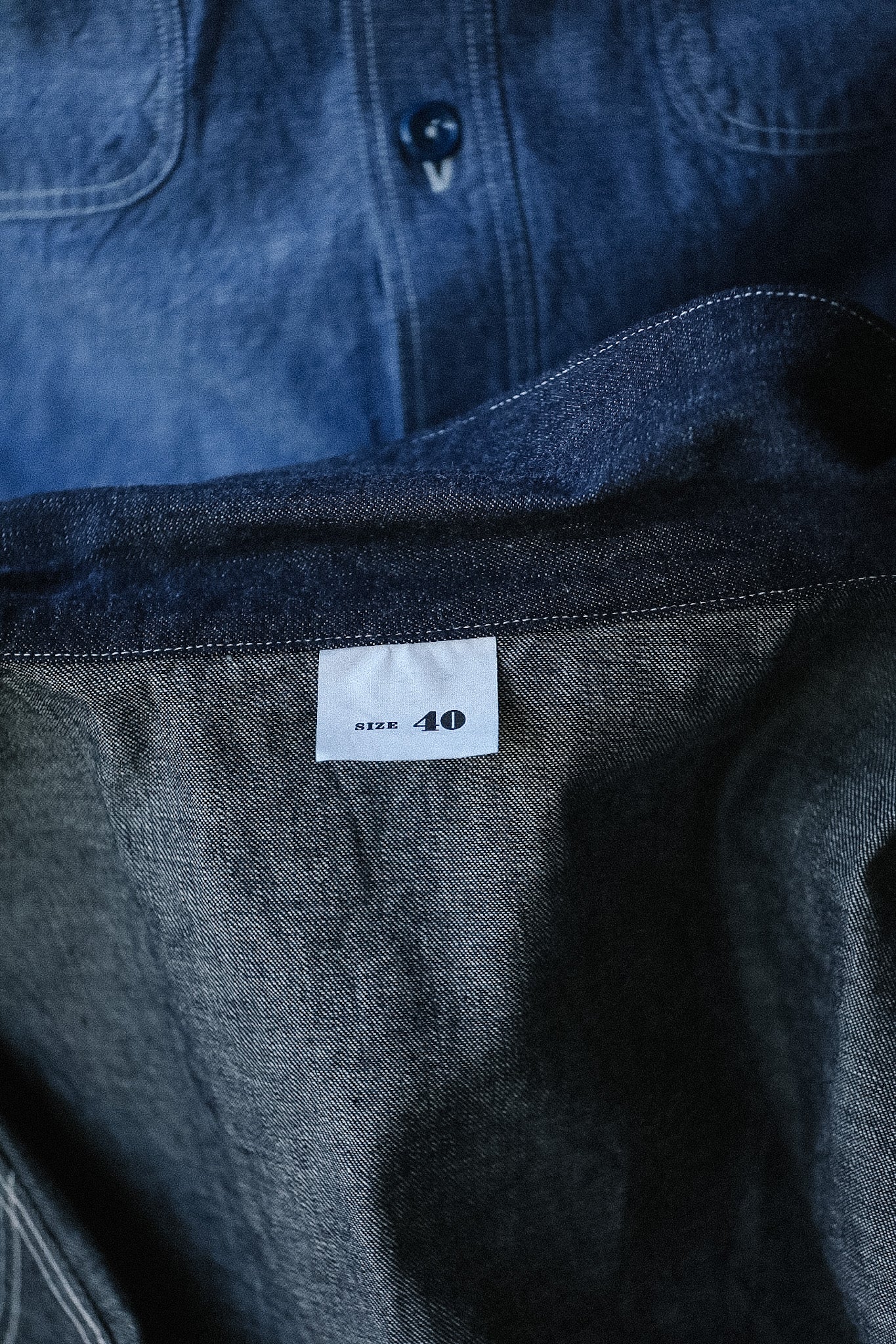 Close-up of a dark denim shirt with a size label on a blurred background