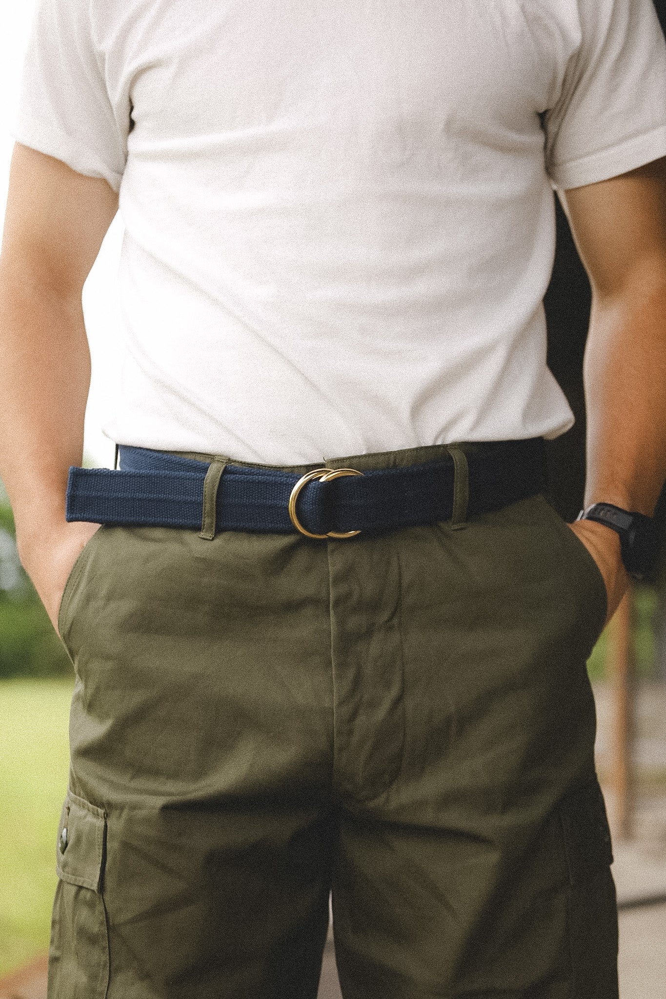 Person wearing a white t-shirt, green pants, and a blue belt with a blurred background