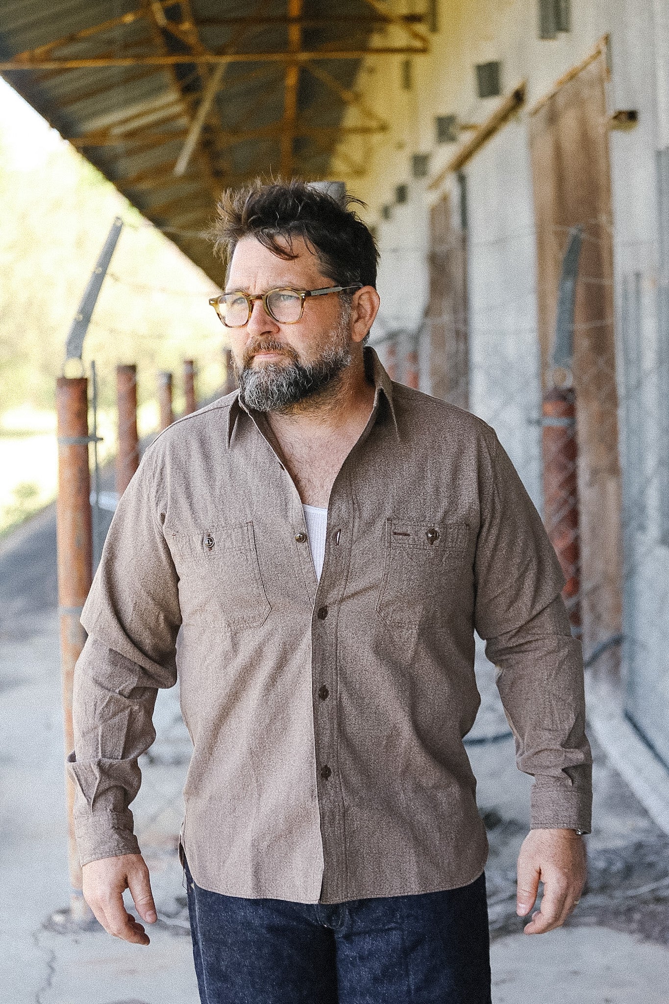 Man wearing a brown shirt and glasses standing in an industrial setting