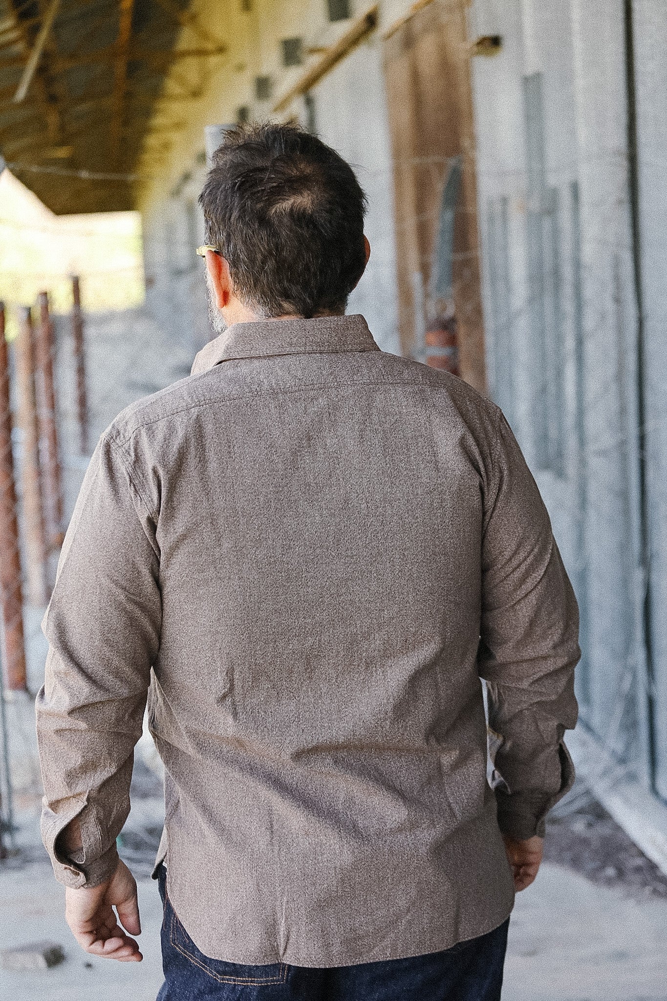 Man wearing a brown jacket walking away from the camera in an urban setting.