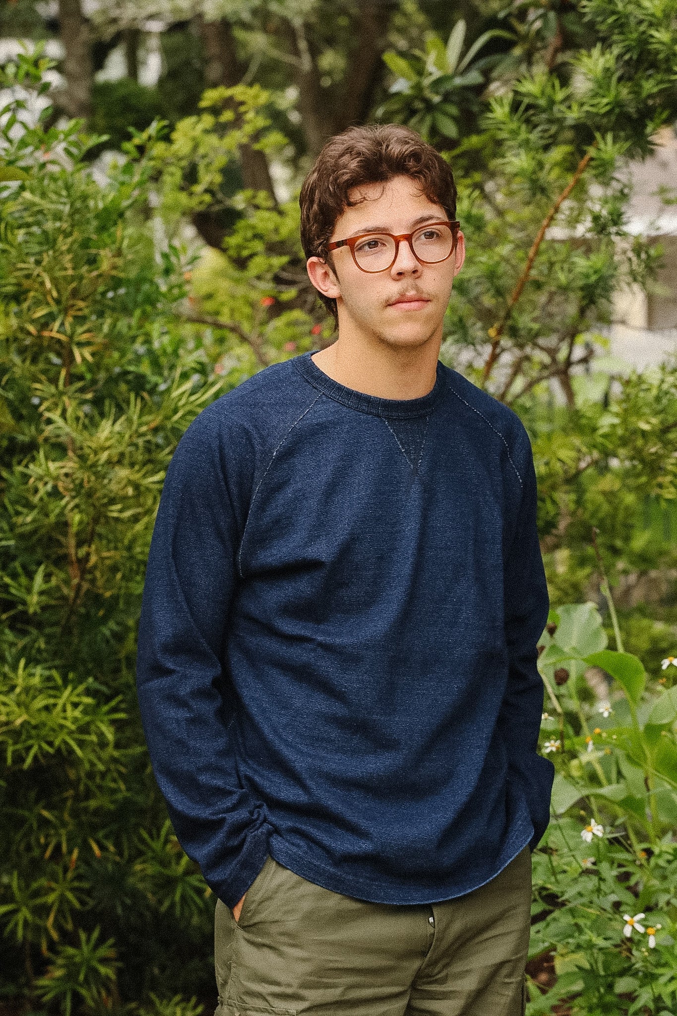 man wearing dark blue long sleeved shirt standing with a green foliage background