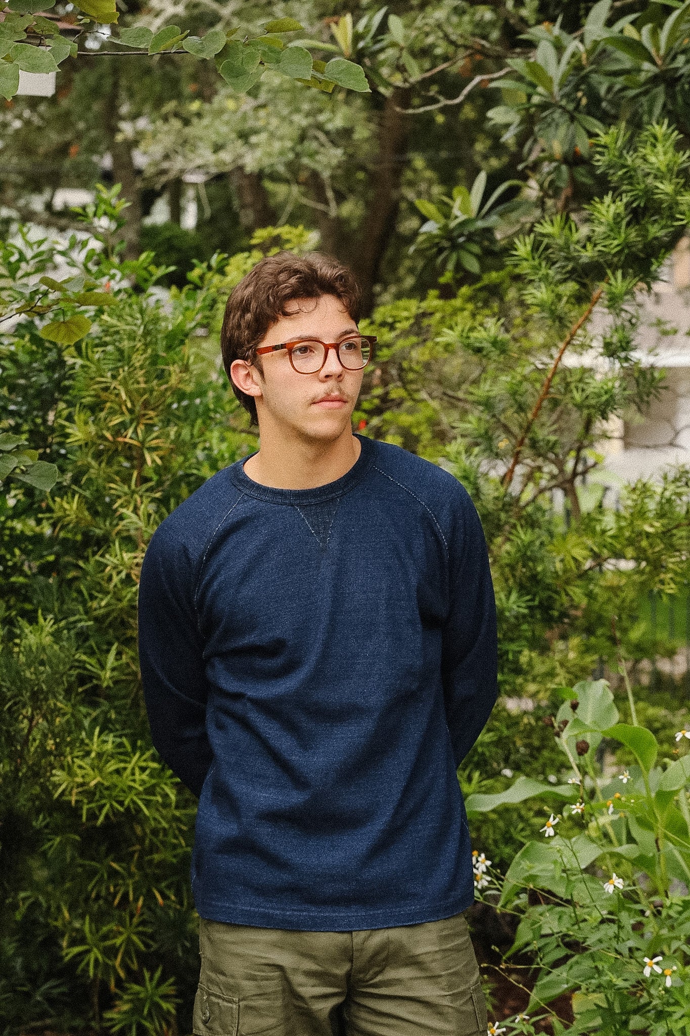 man wearing dark blue long sleeved shirt standing with a green foliage background