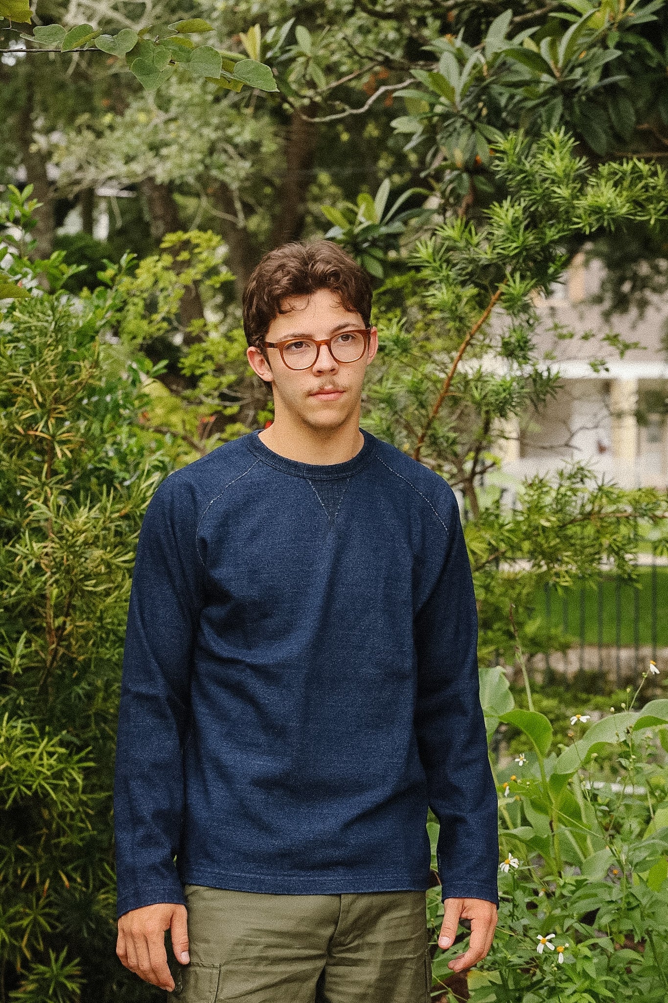 man wearing dark blue long sleeved shirt standing with a green foliage background