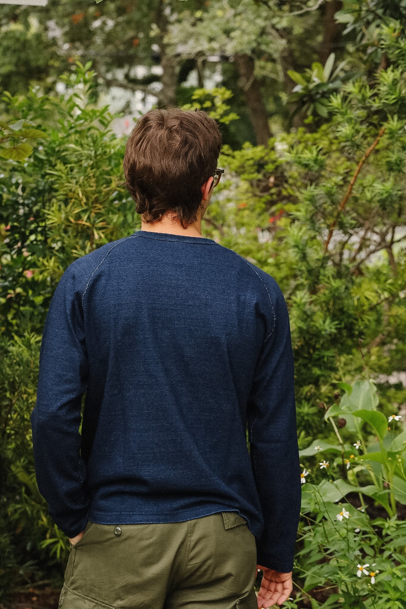 man wearing dark blue long sleeved shirt standing away with a green foliage background