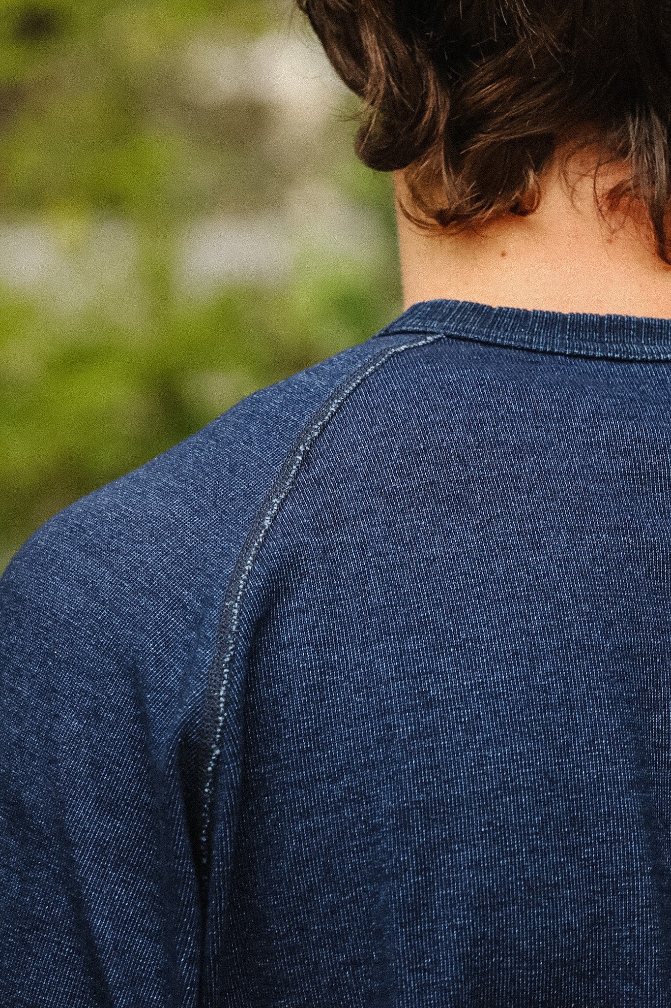 detail shot of a textured blue shirt with a green foliage background. 