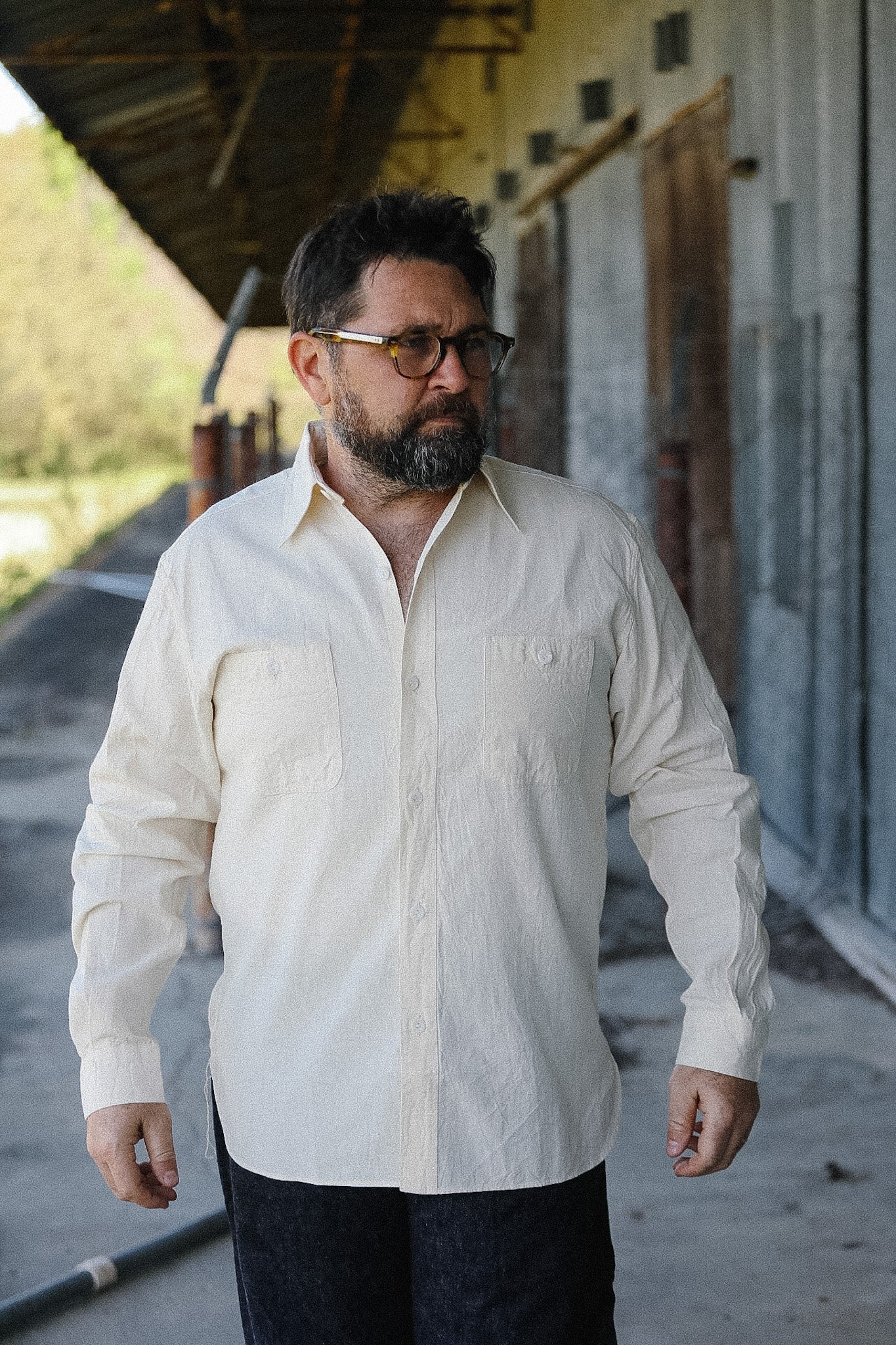Man wearing a light-colored shirt and dark pants standing outdoors.