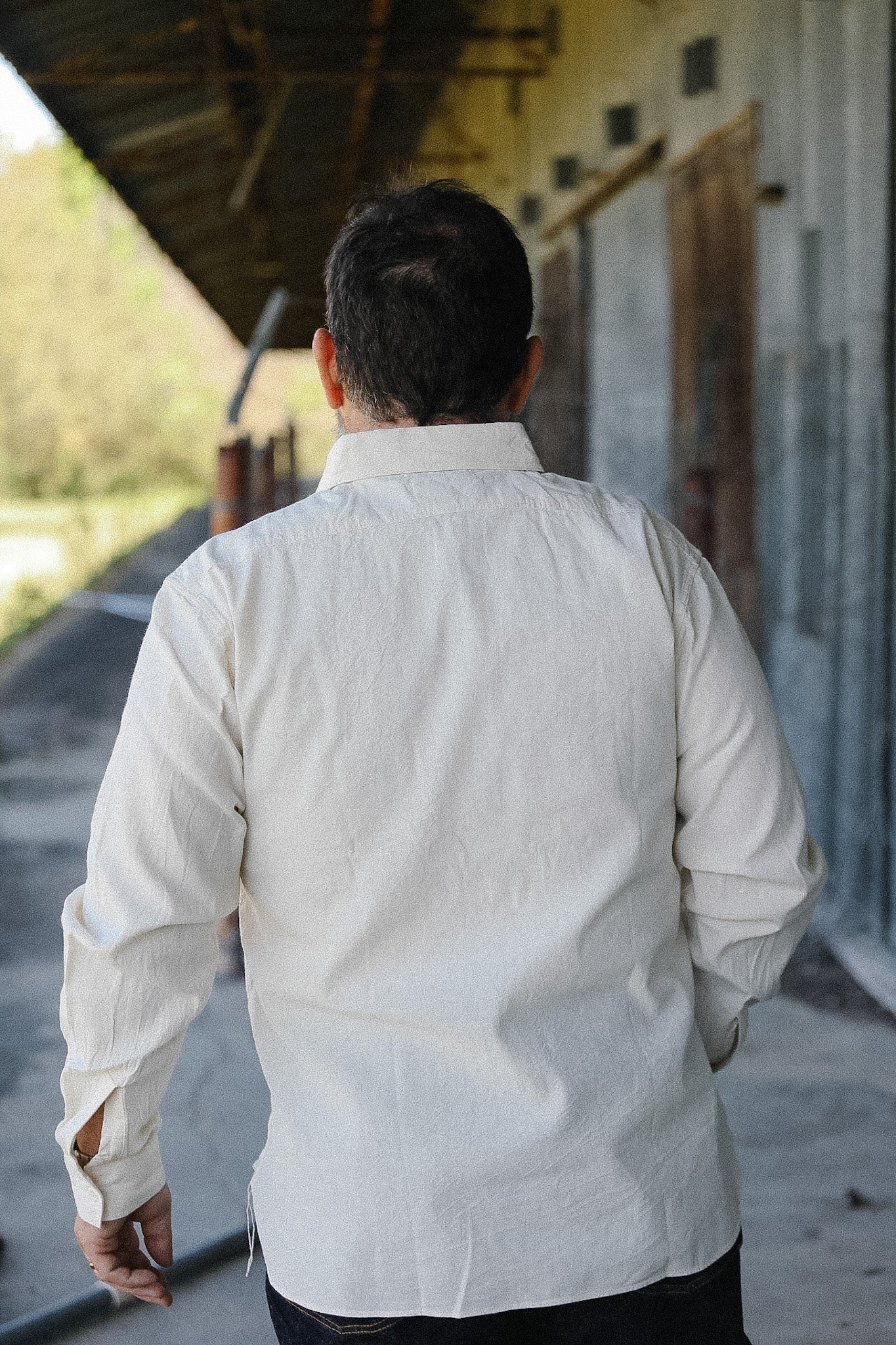 Man wearing a white shirt walking away from the camera in an outdoor setting.