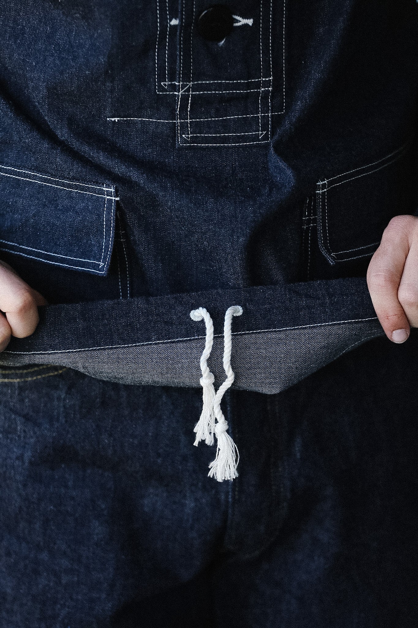 Close-up of a person wearing dark blue denim overalls with a white drawstring.