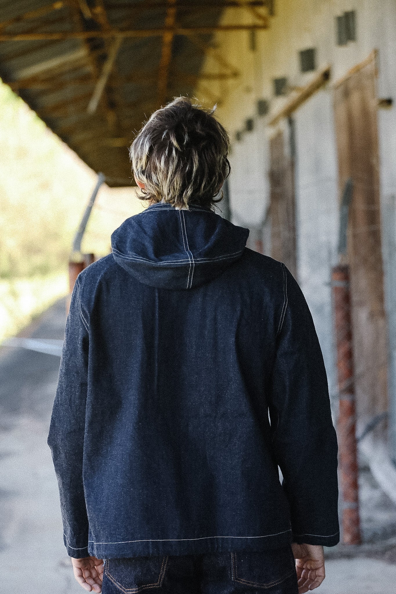Person wearing a dark denim jacket standing under a wooden structure.