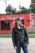 Man wearing a black leather jacket with fur collar and blue baseball cap standing outdoors