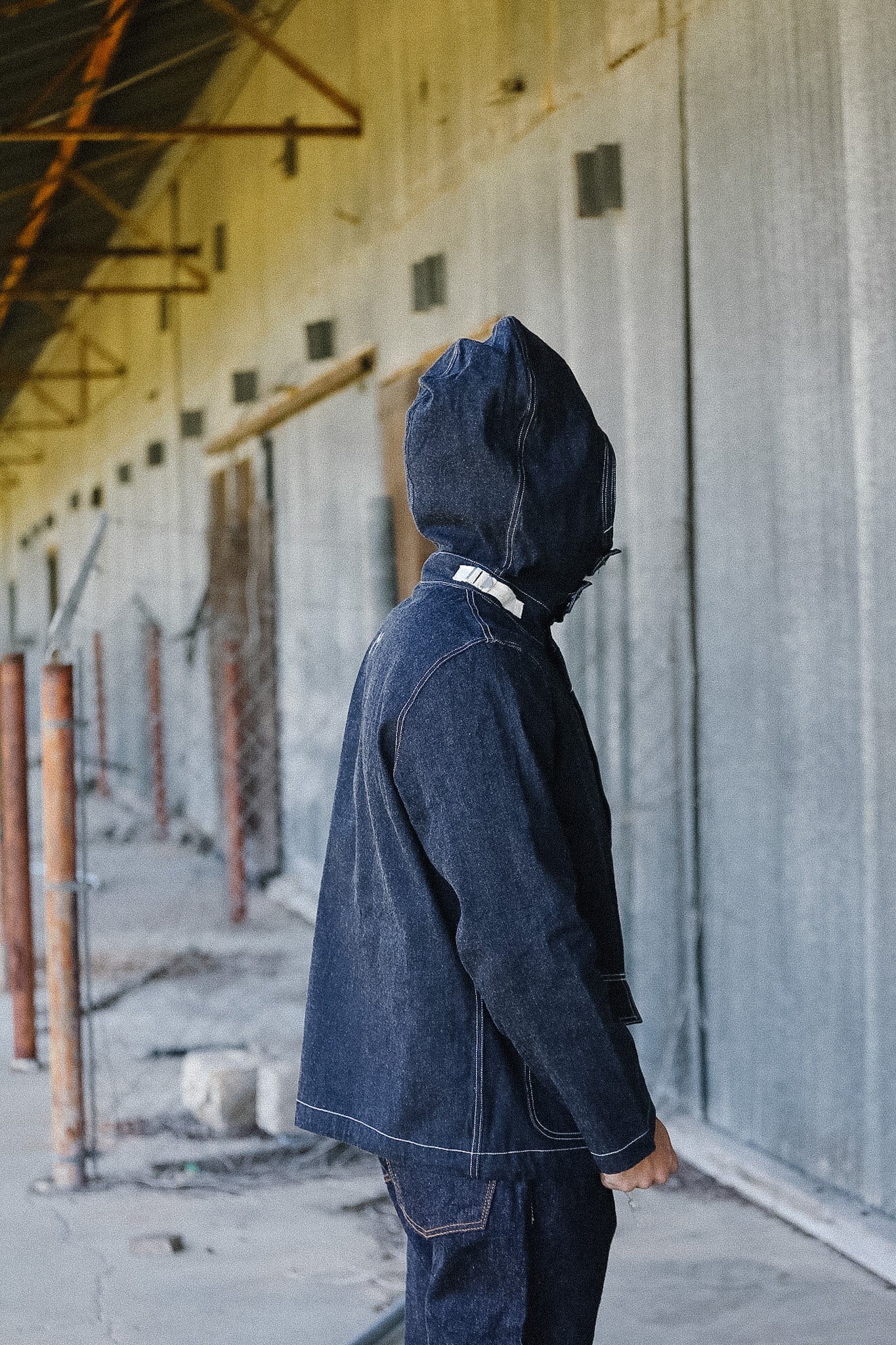 Person wearing a dark denim jacket and pants in an industrial setting