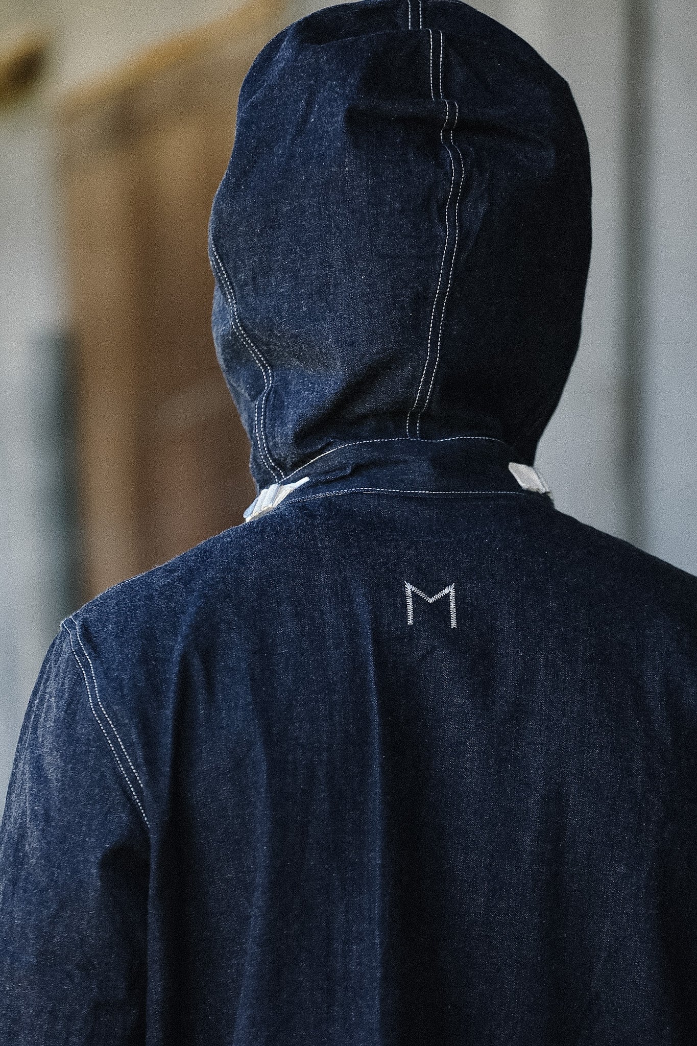 Person wearing a dark blue hoodie with a logo on the back, standing indoors.