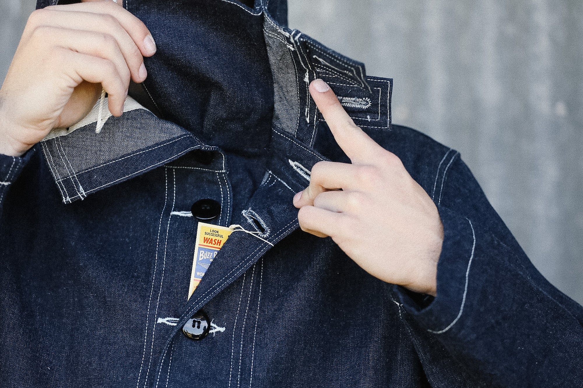 Person adjusting a dark denim jacket with a brand tag visible.