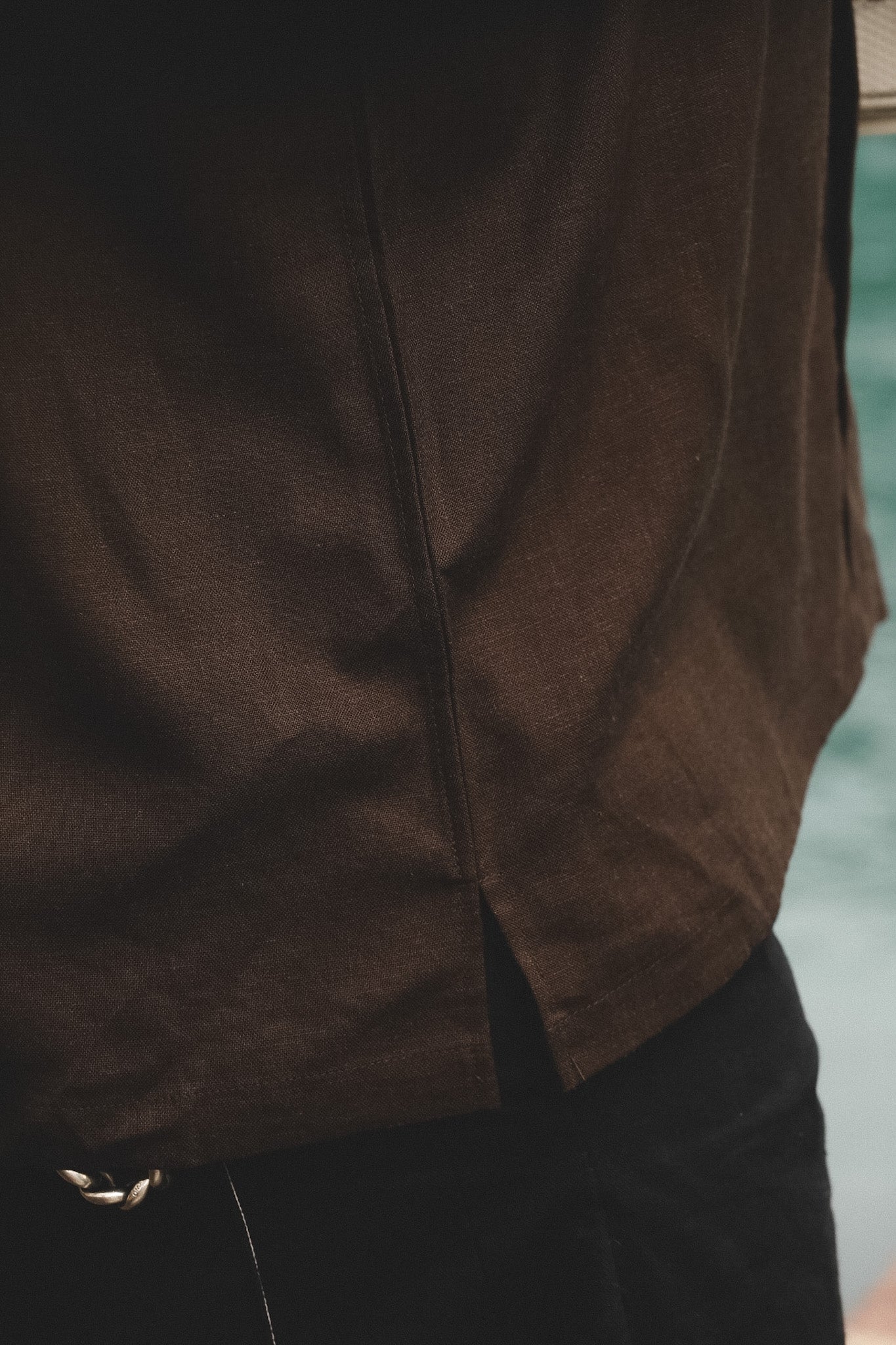 Close-up of a person wearing a dark brown textured shirt and black pants, with a blurred outdoor background.