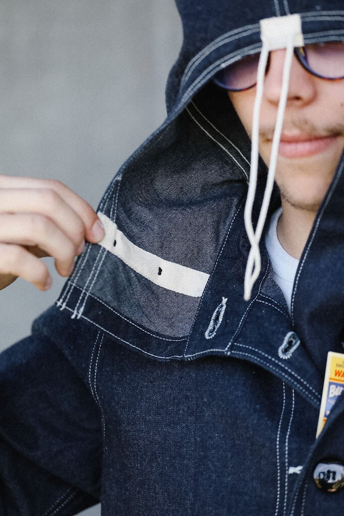 Person wearing a blue denim jacket with a hood, smiling.