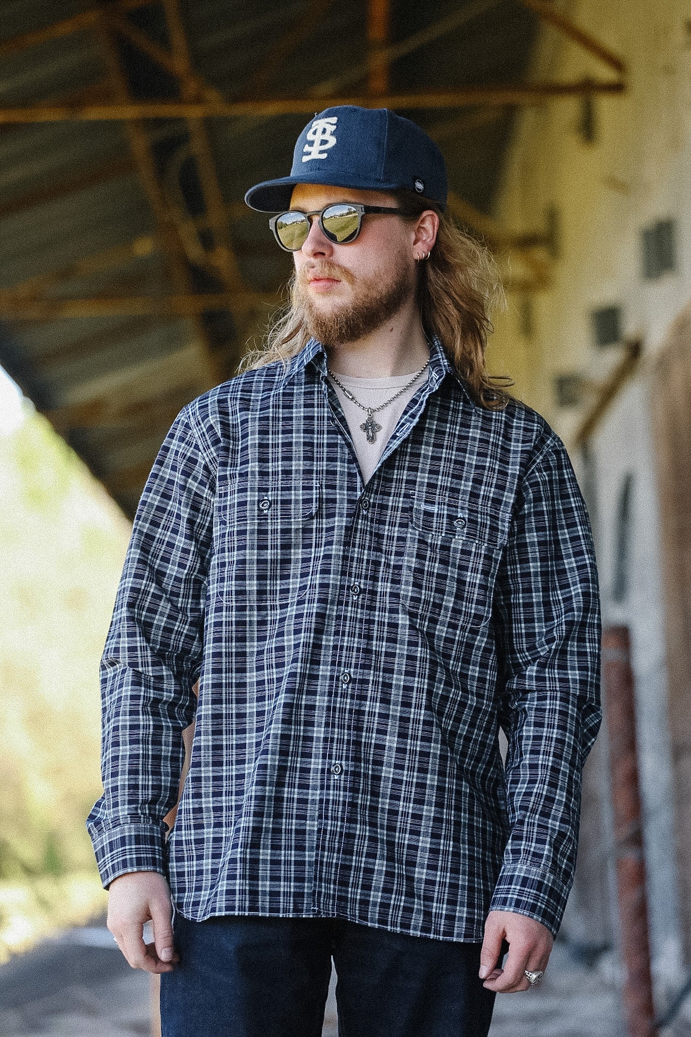 Man wearing a plaid shirt and cap standing in an industrial setting