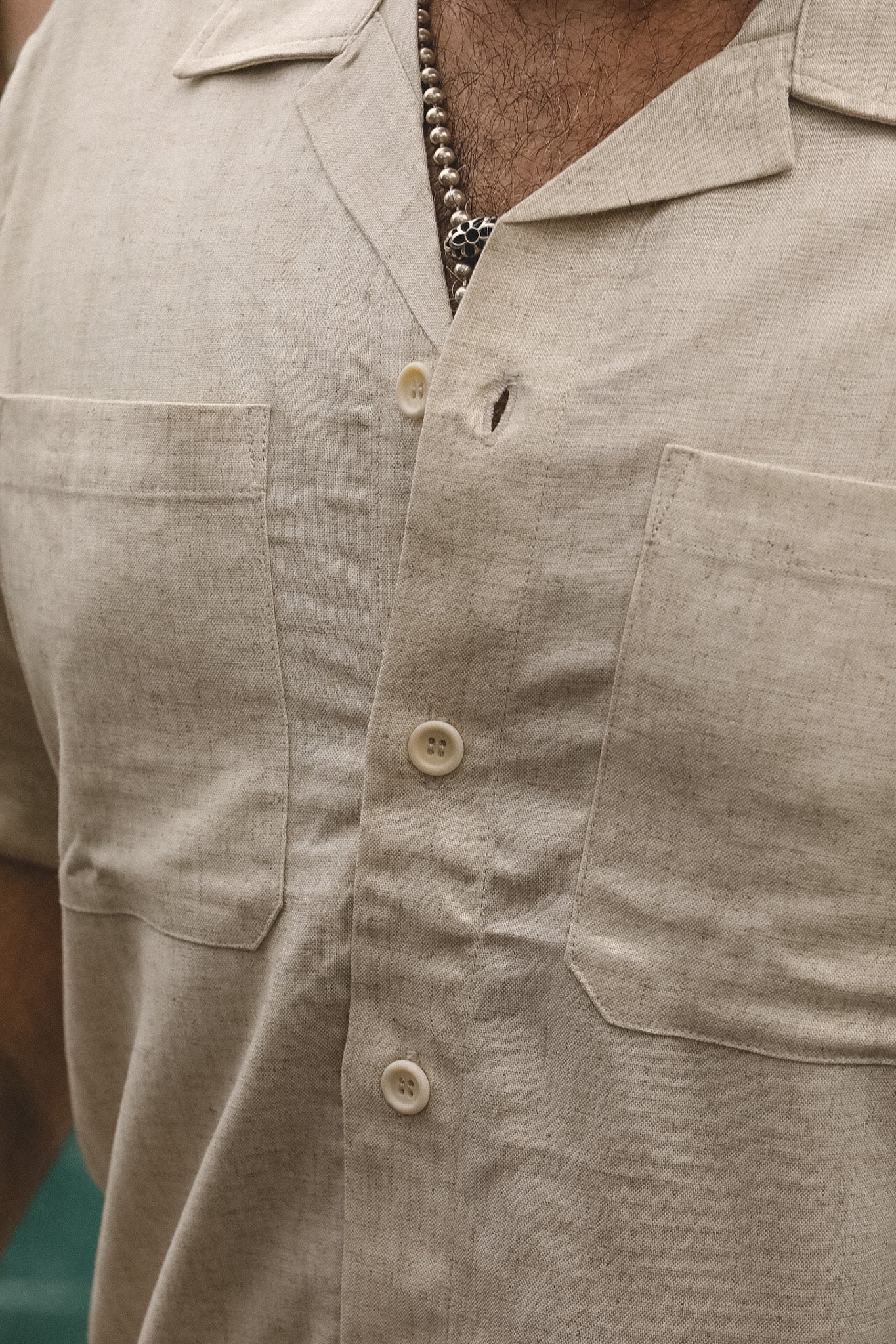 Close-up of a man wearing a light beige linen short-sleeve button-up shirt with two chest pockets and cream-colored buttons.