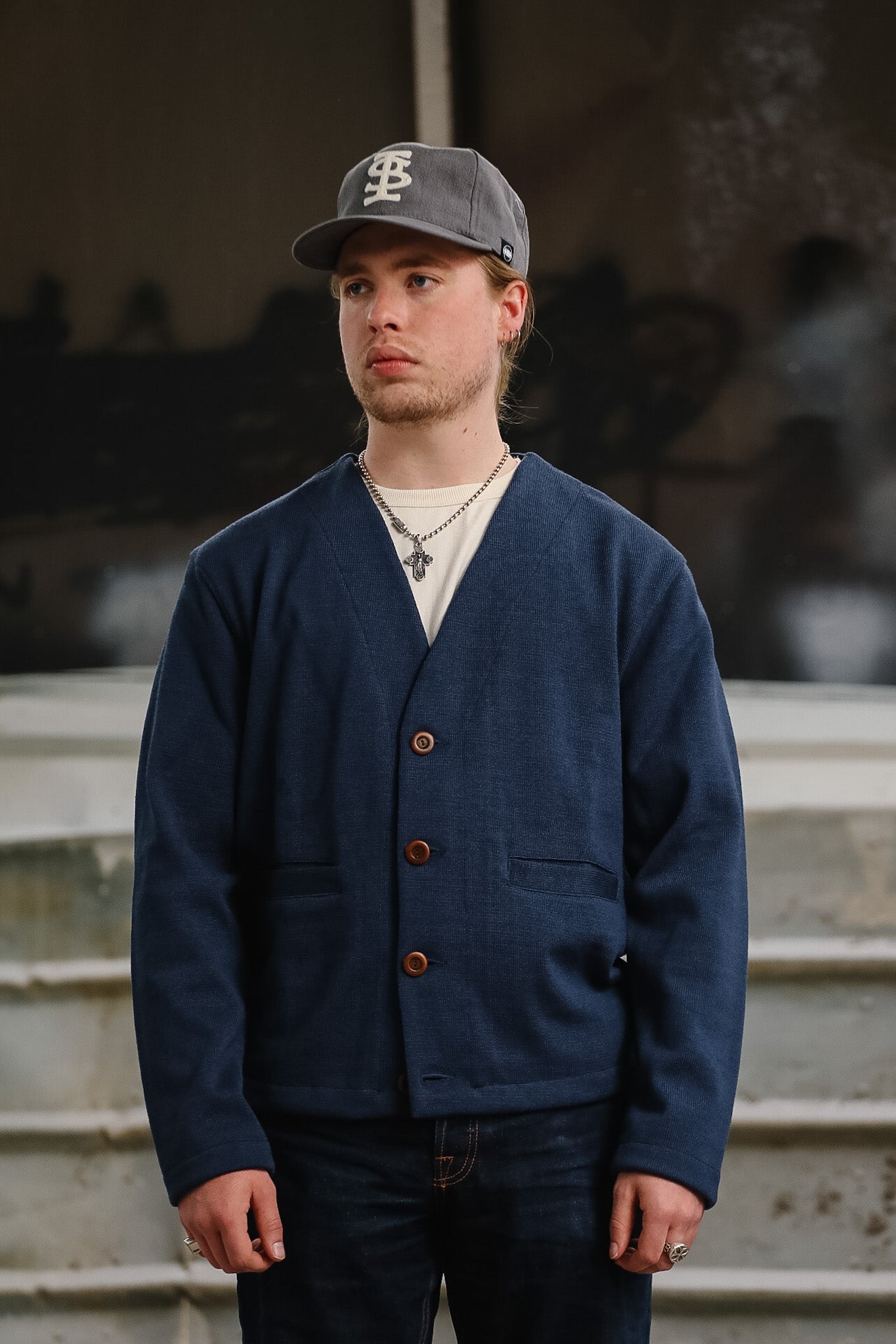 Man wearing a navy cardigan and gray cap standing on steps with a blurred background