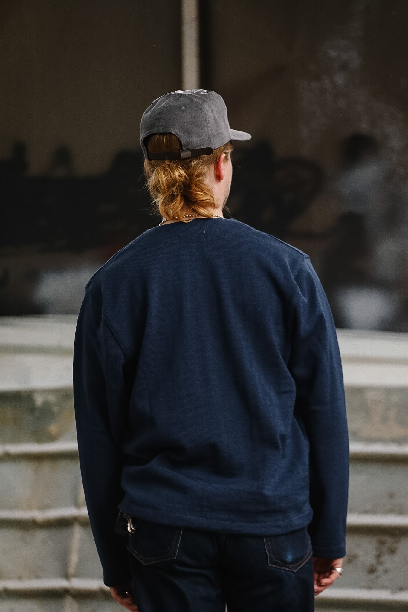 Person wearing a navy sweatshirt and gray cap standing on steps with a blurred background