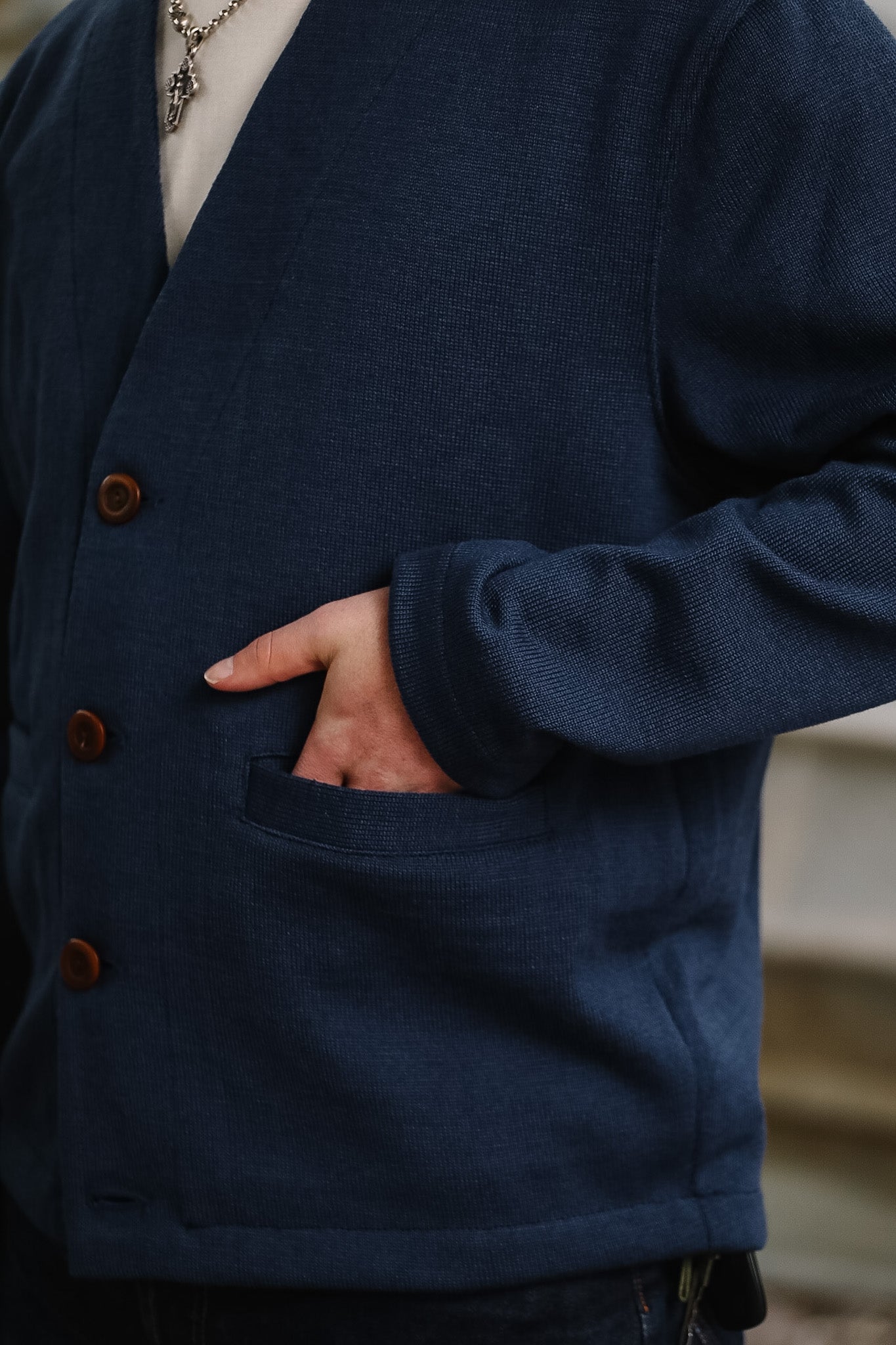 Person wearing a navy blue cardigan with brown buttons, standing against a blurred background.