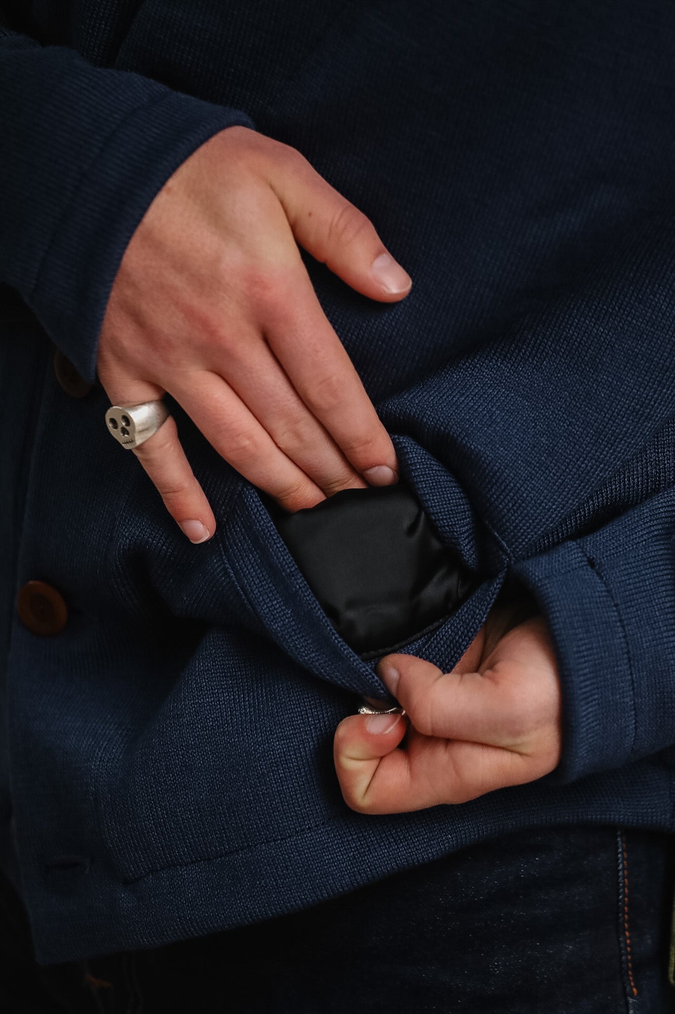 Person wearing a navy blue coat with a close-up of their hand adjusting the collar.