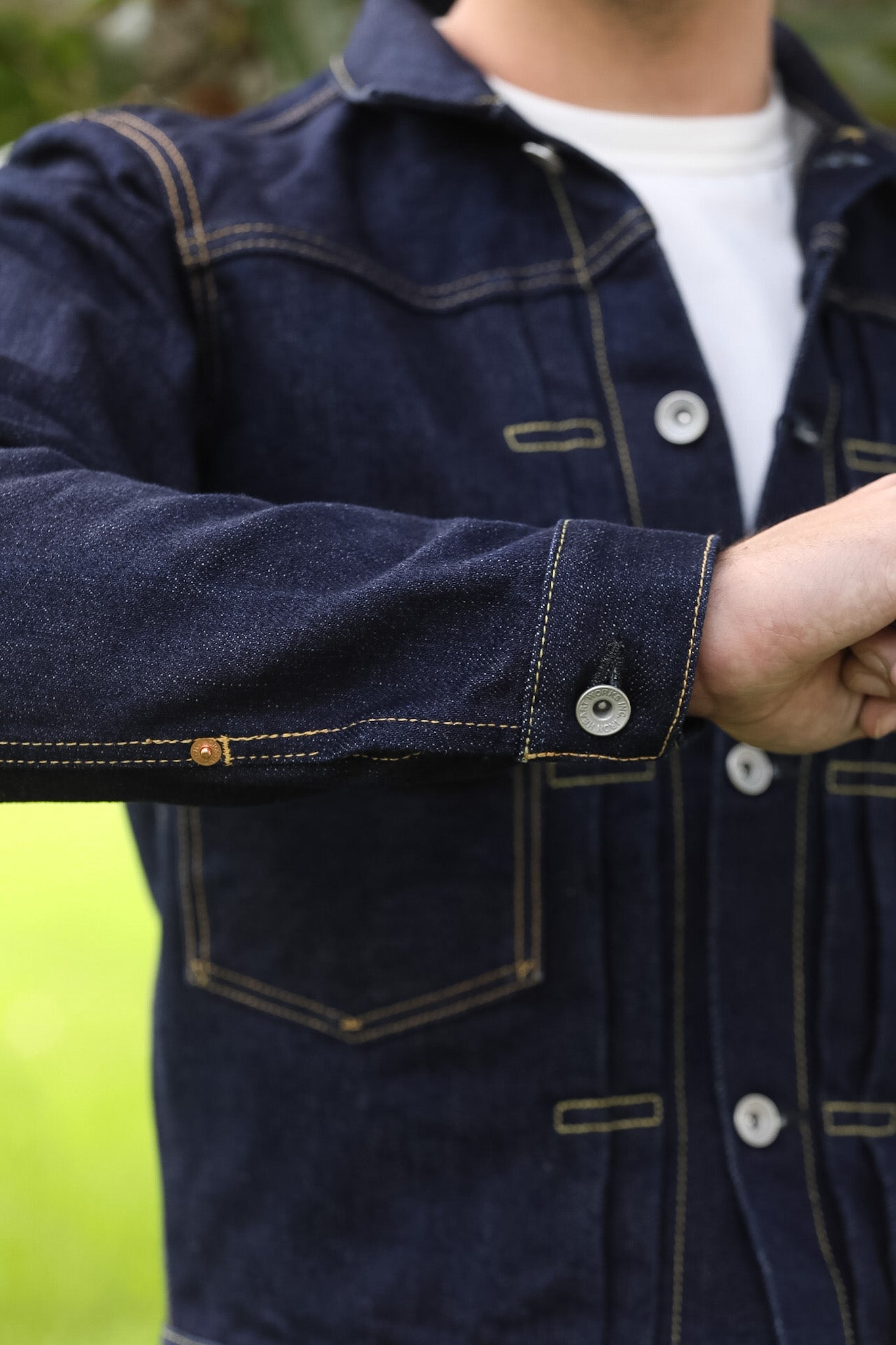 A close-up of a person wearing a dark indigo denim jacket over a white t-shirt, showing the sleeve and front pocket details.