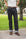 A person standing outdoors on a sidewalk wearing dark indigo denim jeans with a brown belt and brown shoes, with a white t-shirt partially visible.