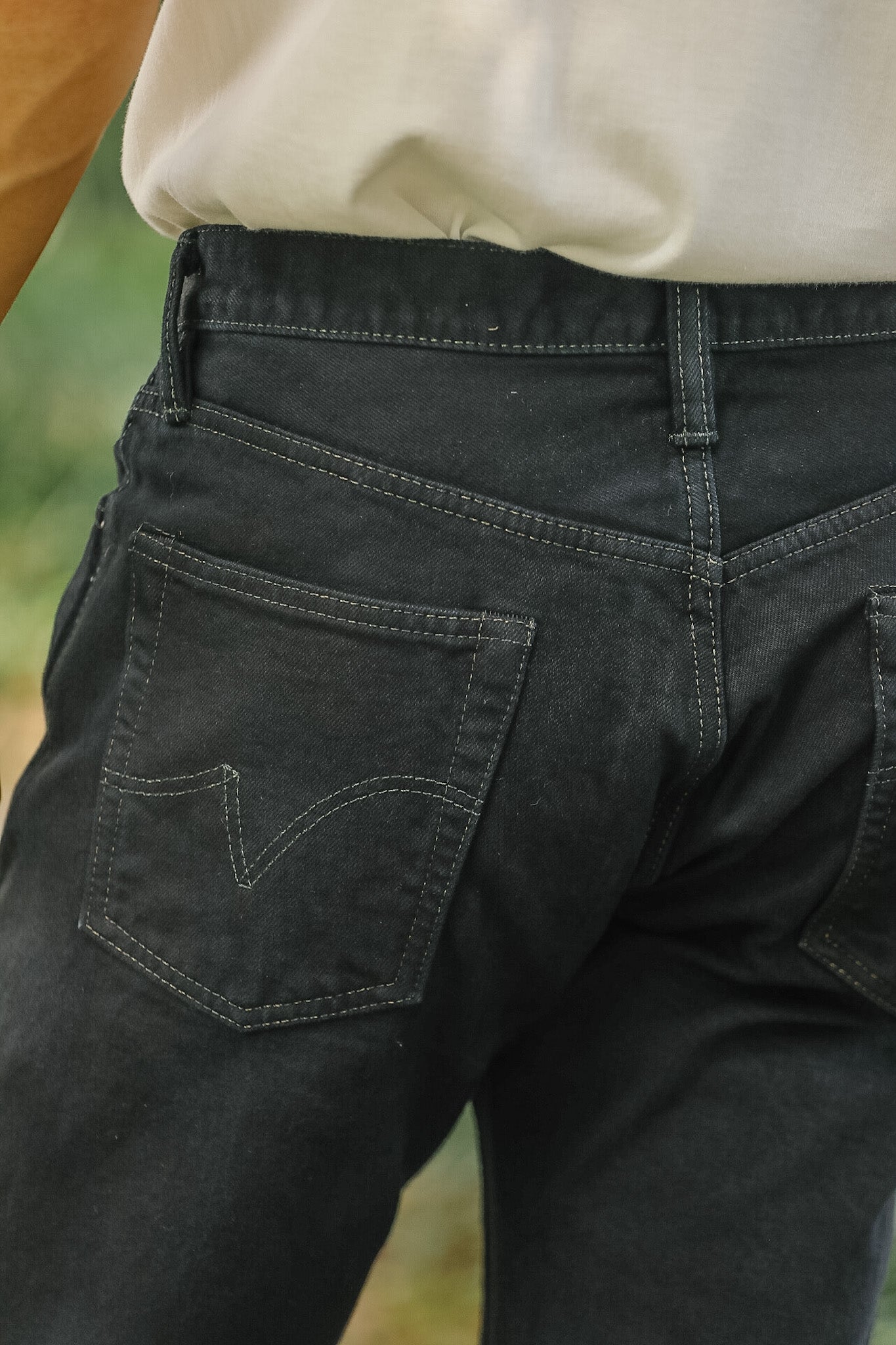 Close-up of the back waistband and rear pocket of black denim jeans worn by a person, with part of a light-colored shirt visible at the top.