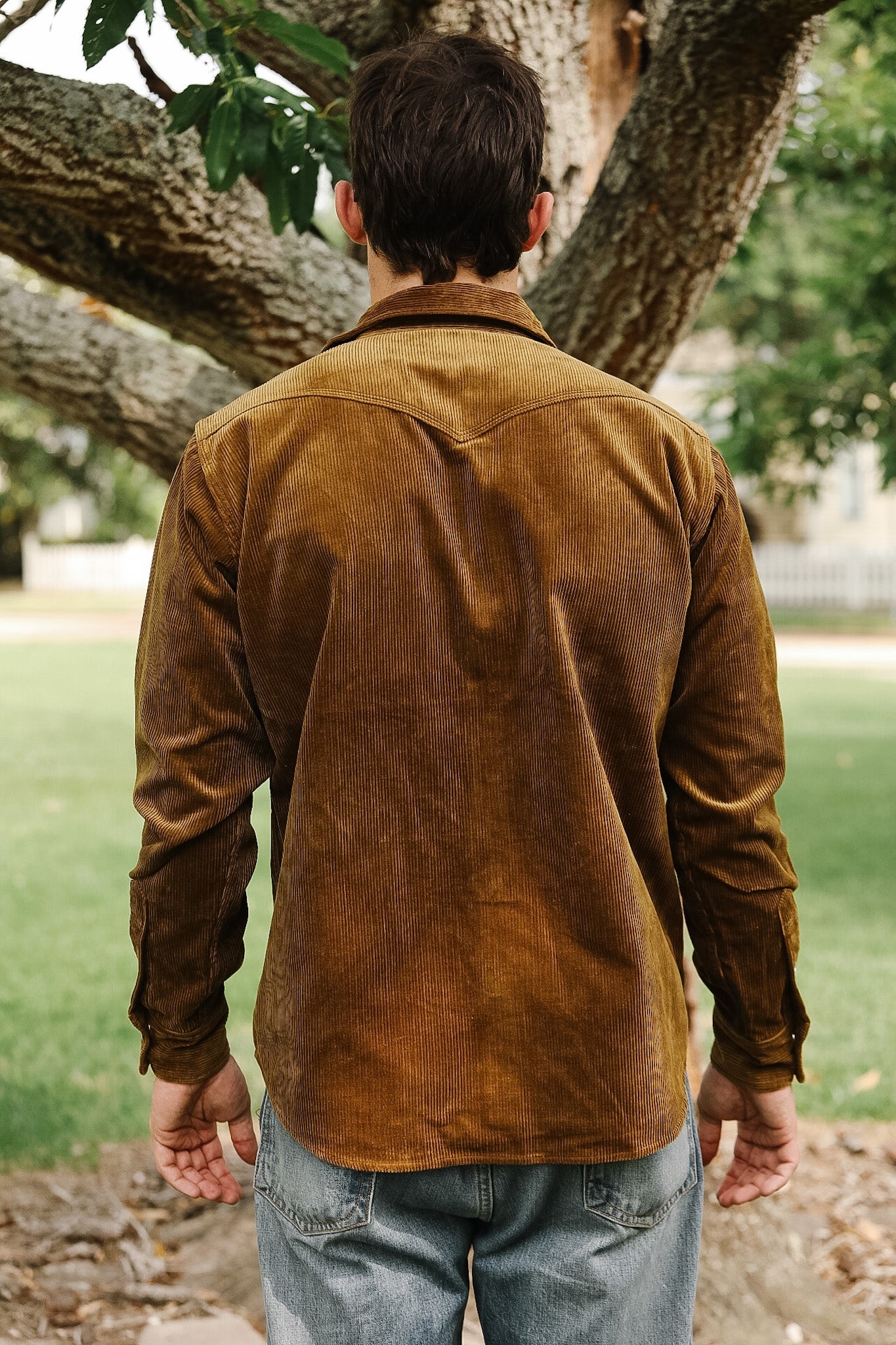 Man wearing a brown corduroy shirt standing outdoors with trees and grass in the background