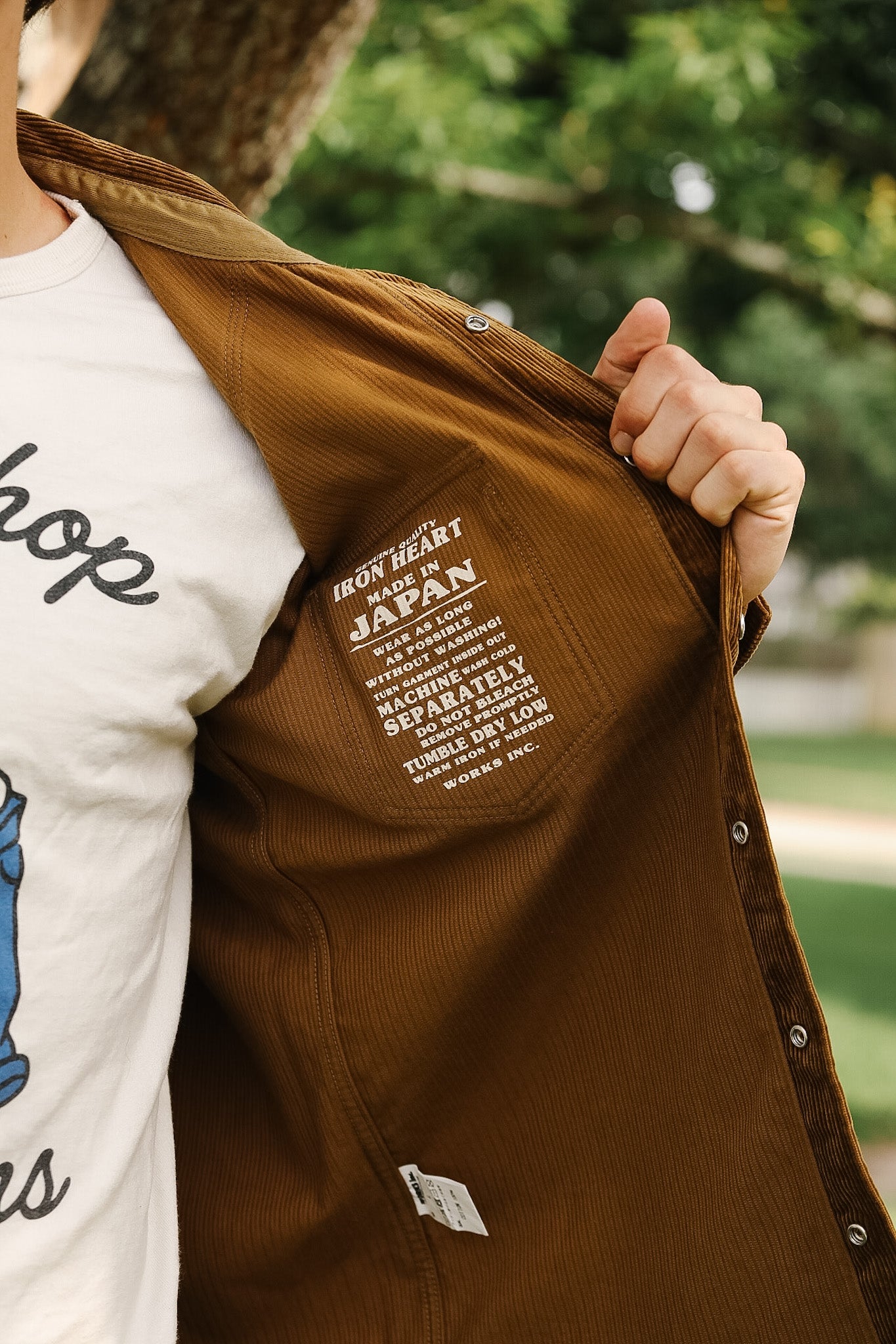 Person wearing a white t-shirt with text and holding a brown jacket with text.