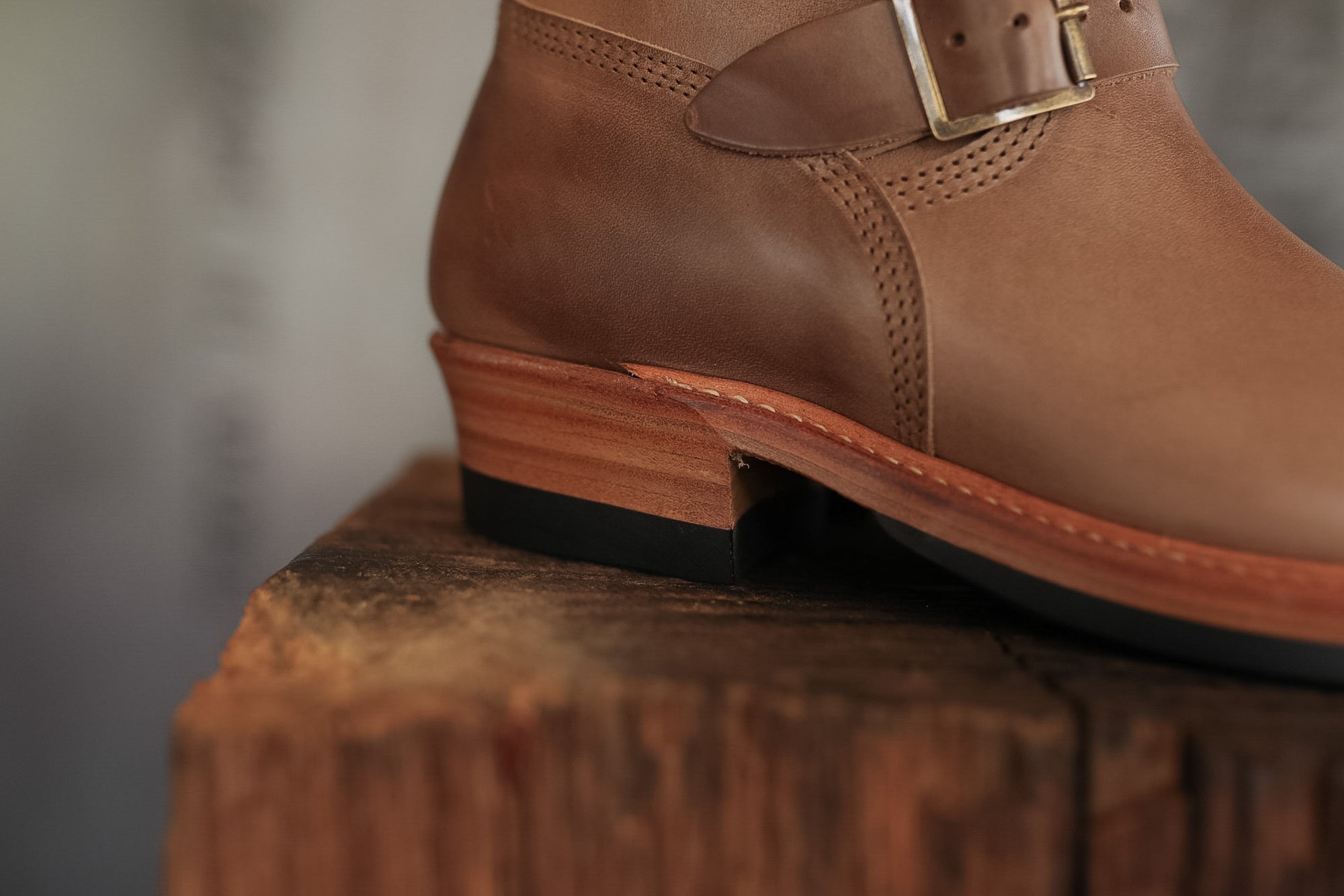 Brown leather boot with a buckle on a wooden block against a blurred background